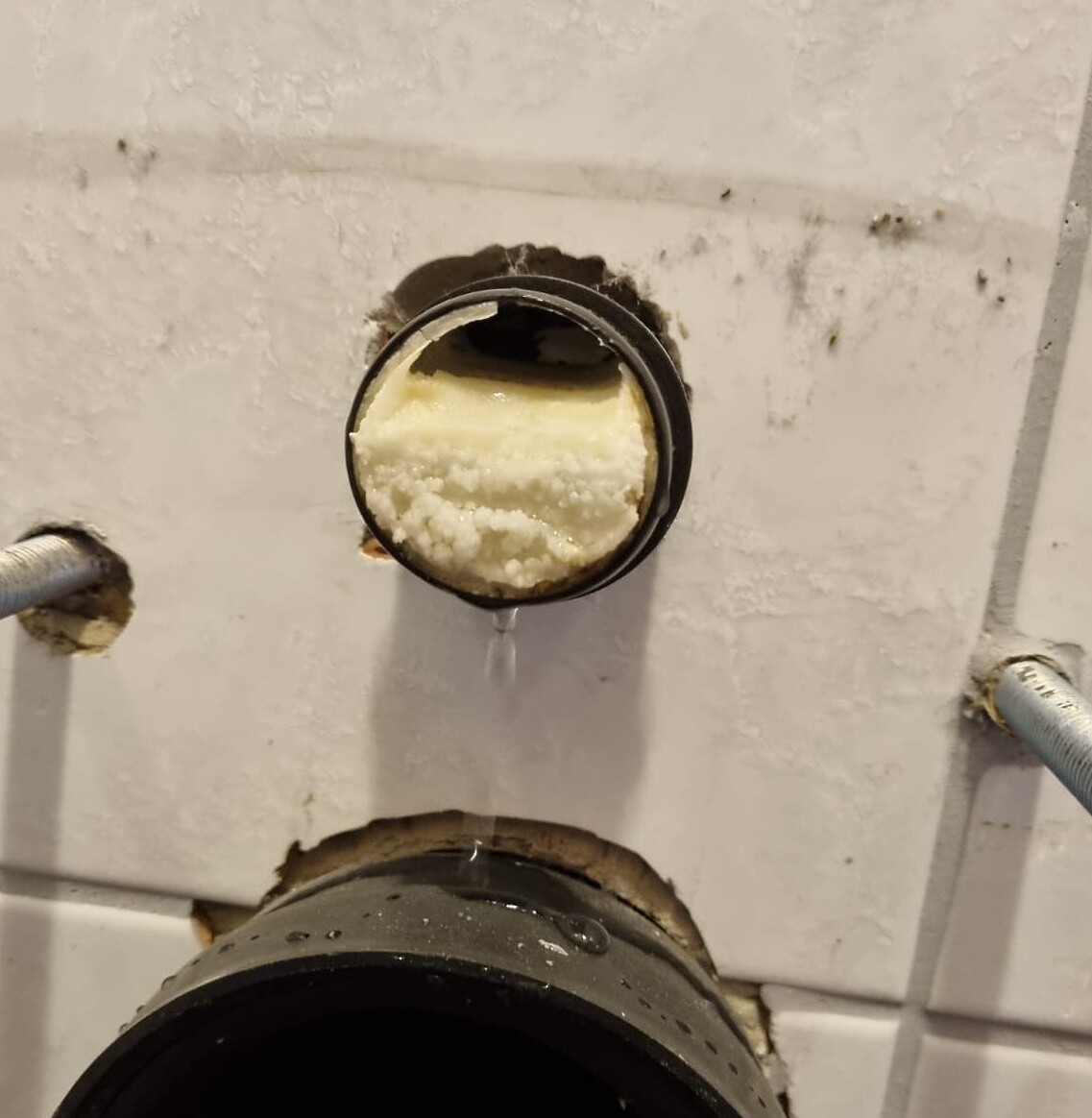 Open sanitary pipe with foam seal, water dripping from the connection before tiling.