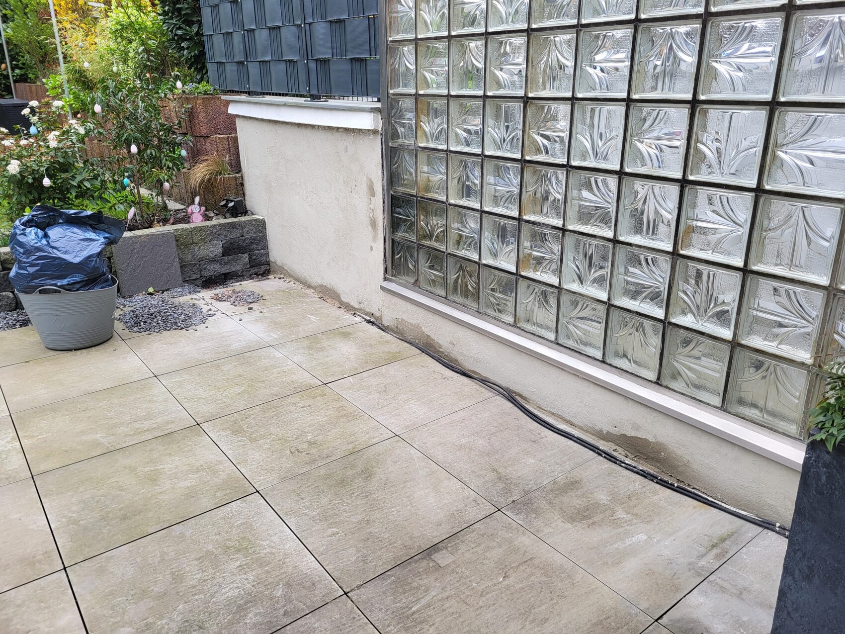 Terrace with beige tiles, glass block wall on the right, planter with blue bag on the left.