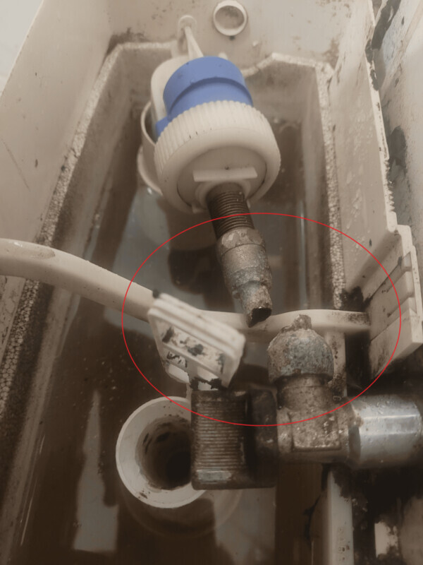 Rusty fitting and hose connection in the cistern of a toilet.