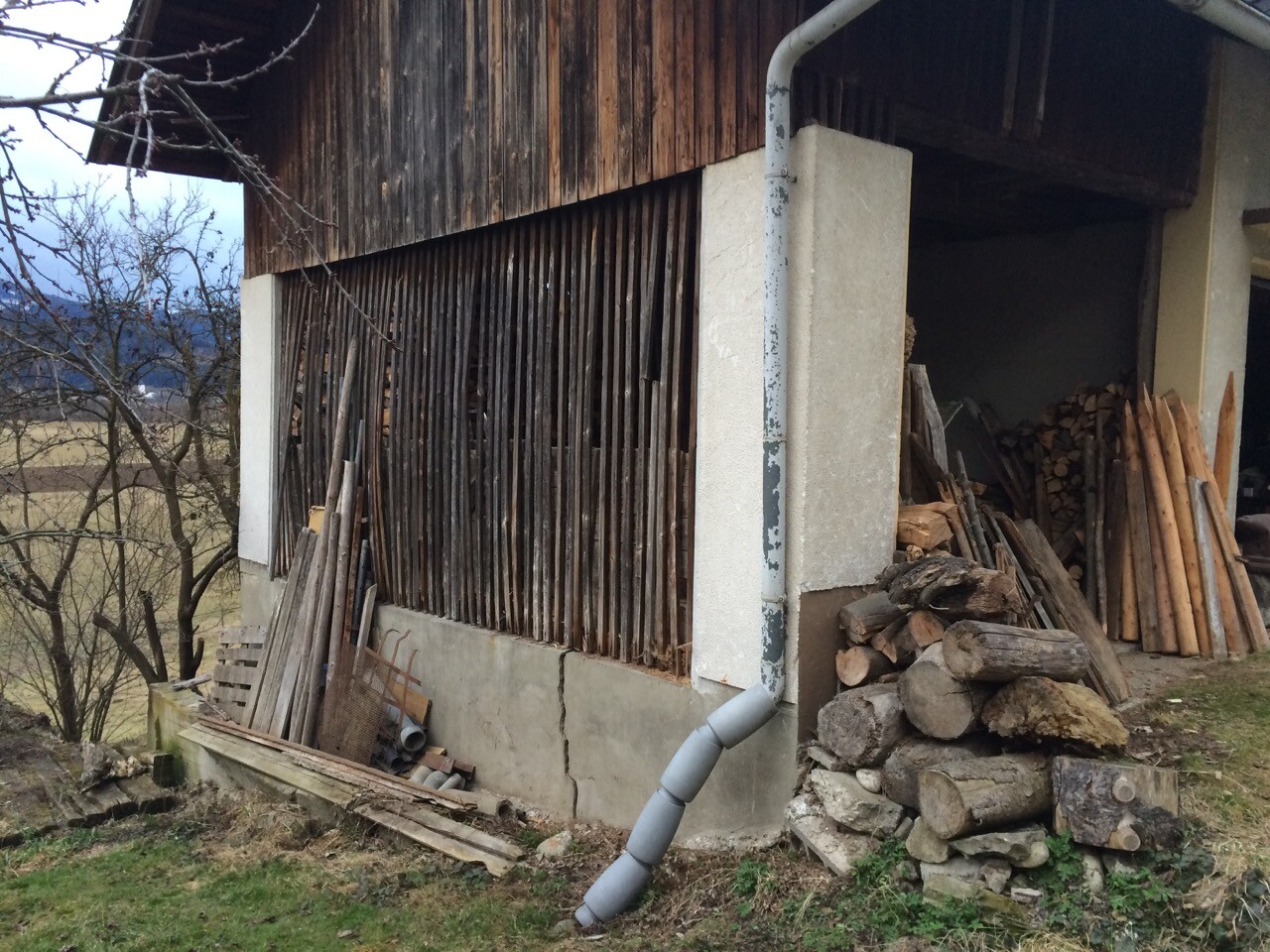 Außenansicht eines Holzhauses mit Holzverkleidung, Holzstapeln und Fallrohr