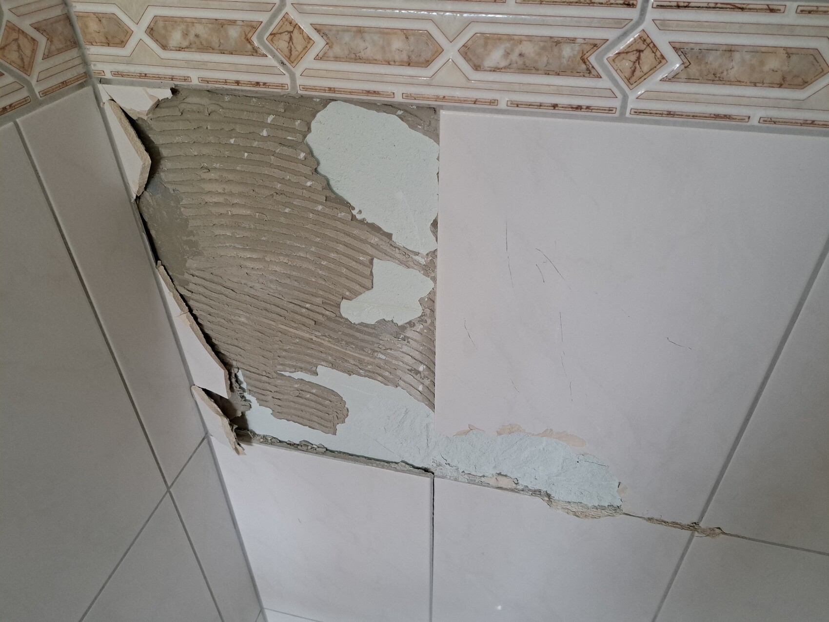 Damage on bathroom wall: peeling plaster behind tiles, exposed plaster texture.