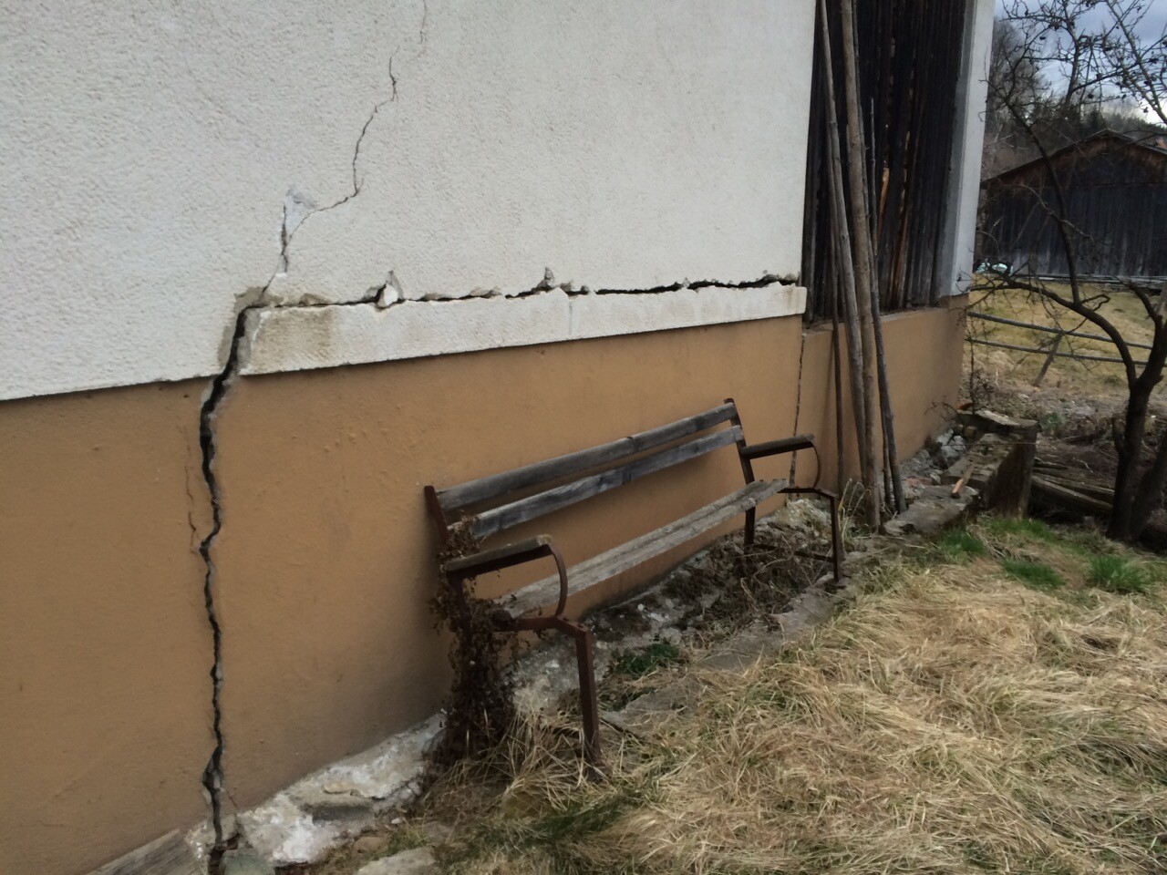 Außenwand mit großem Riss, Putzbruch und verrosteter Bank davor.
