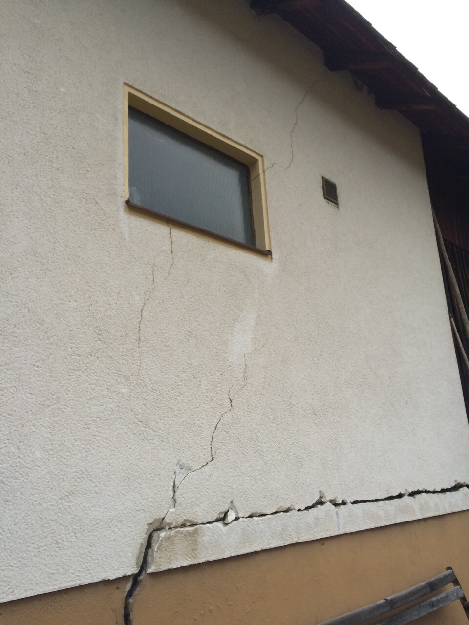 Außenwand eines Hauses mit sichtbaren Rissen und beschädigtem Verputz.
