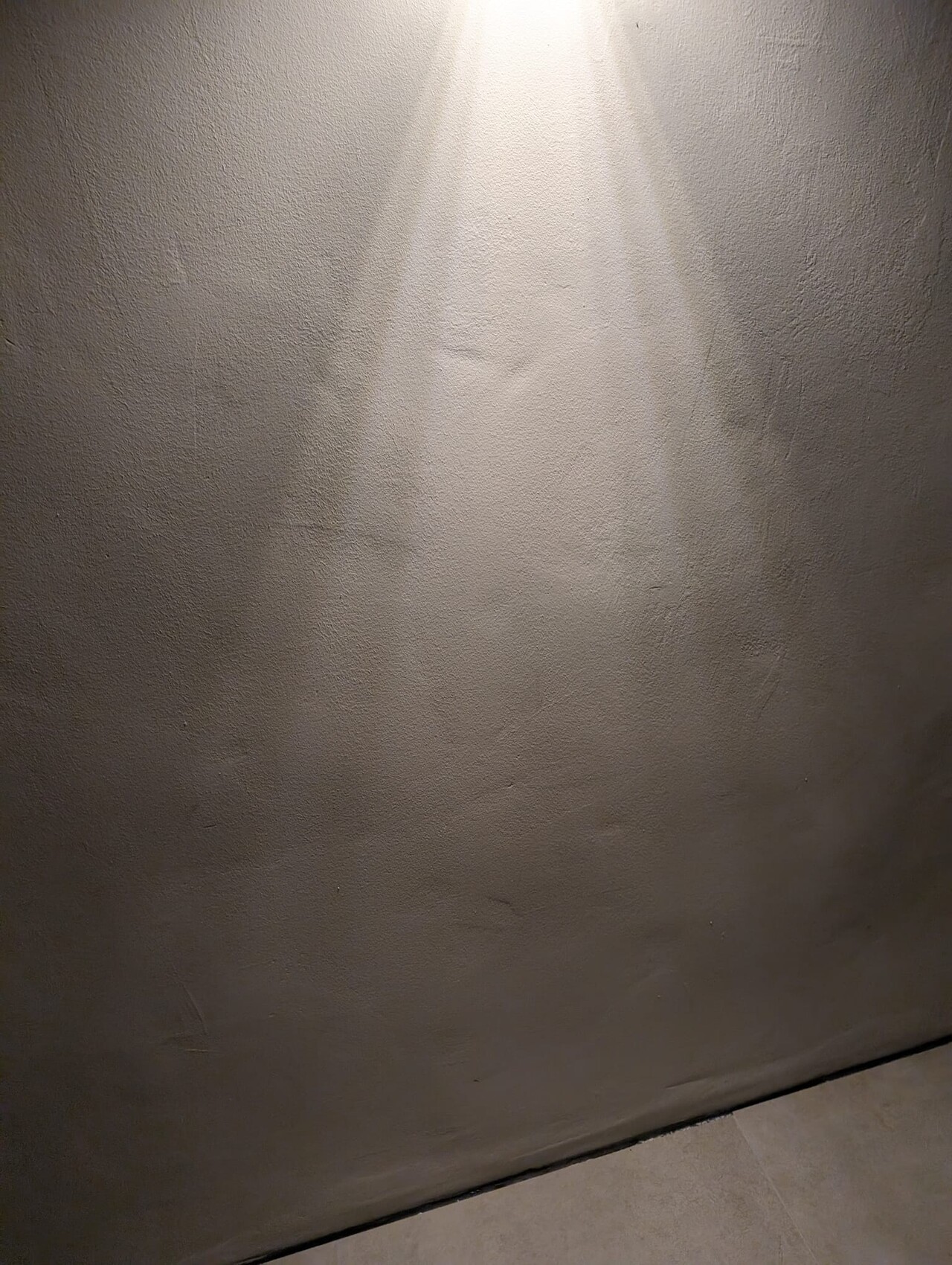 Gray plastered interior wall with beam of light from above; floor tiles visible at the bottom.