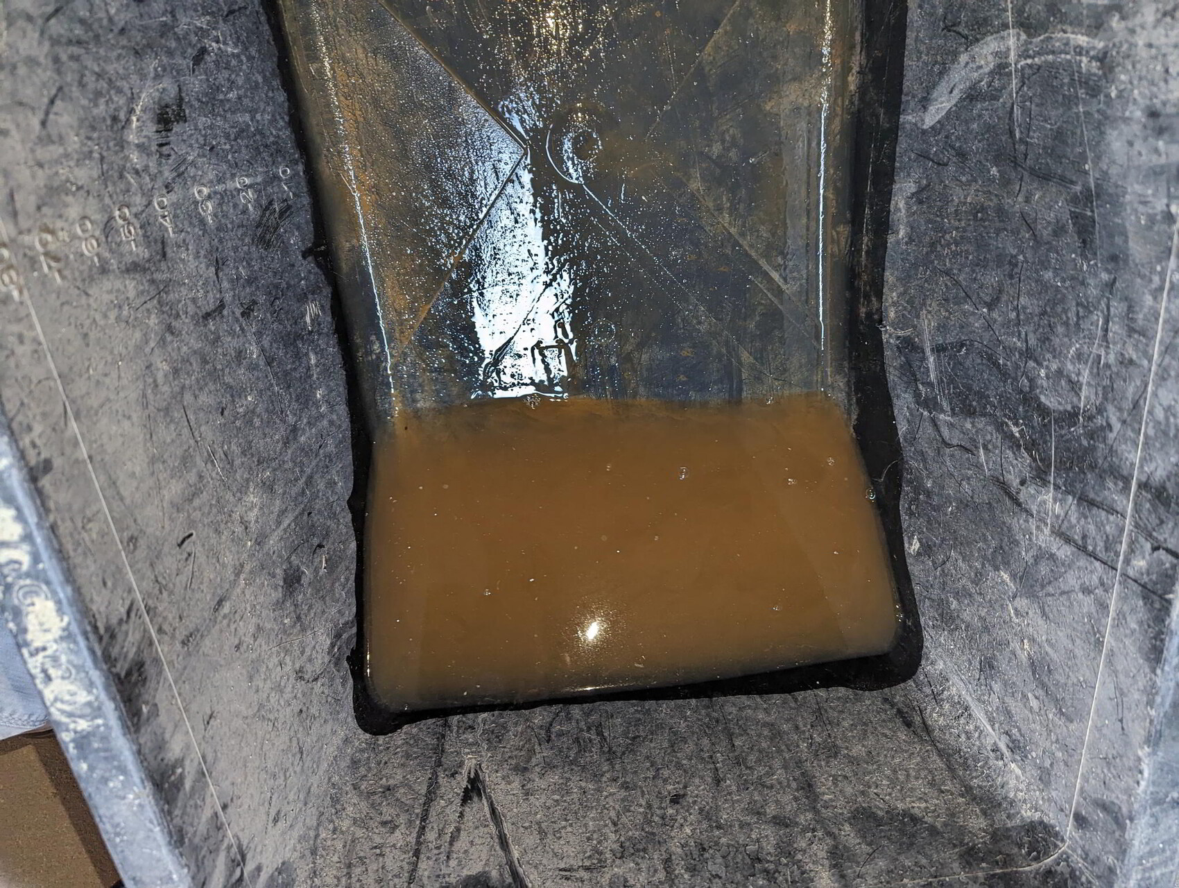 Metal container with brown, cloudy water and sediment at the bottom.