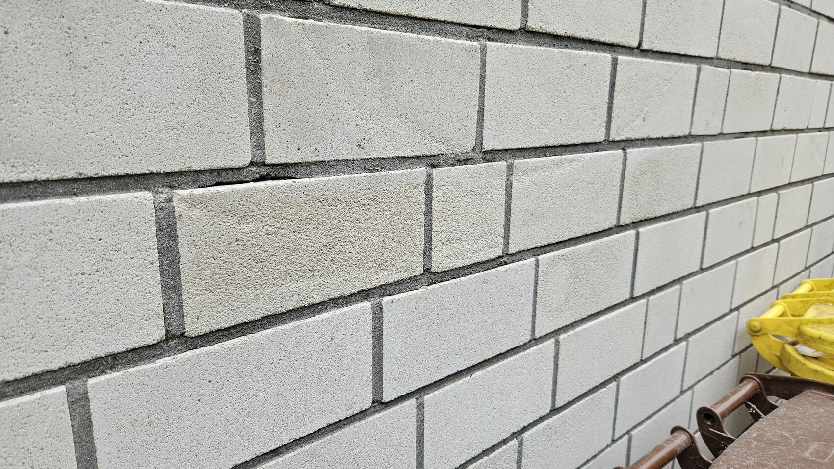 Gray concrete block wall with distinct joints; yellow construction equipment at the bottom right.