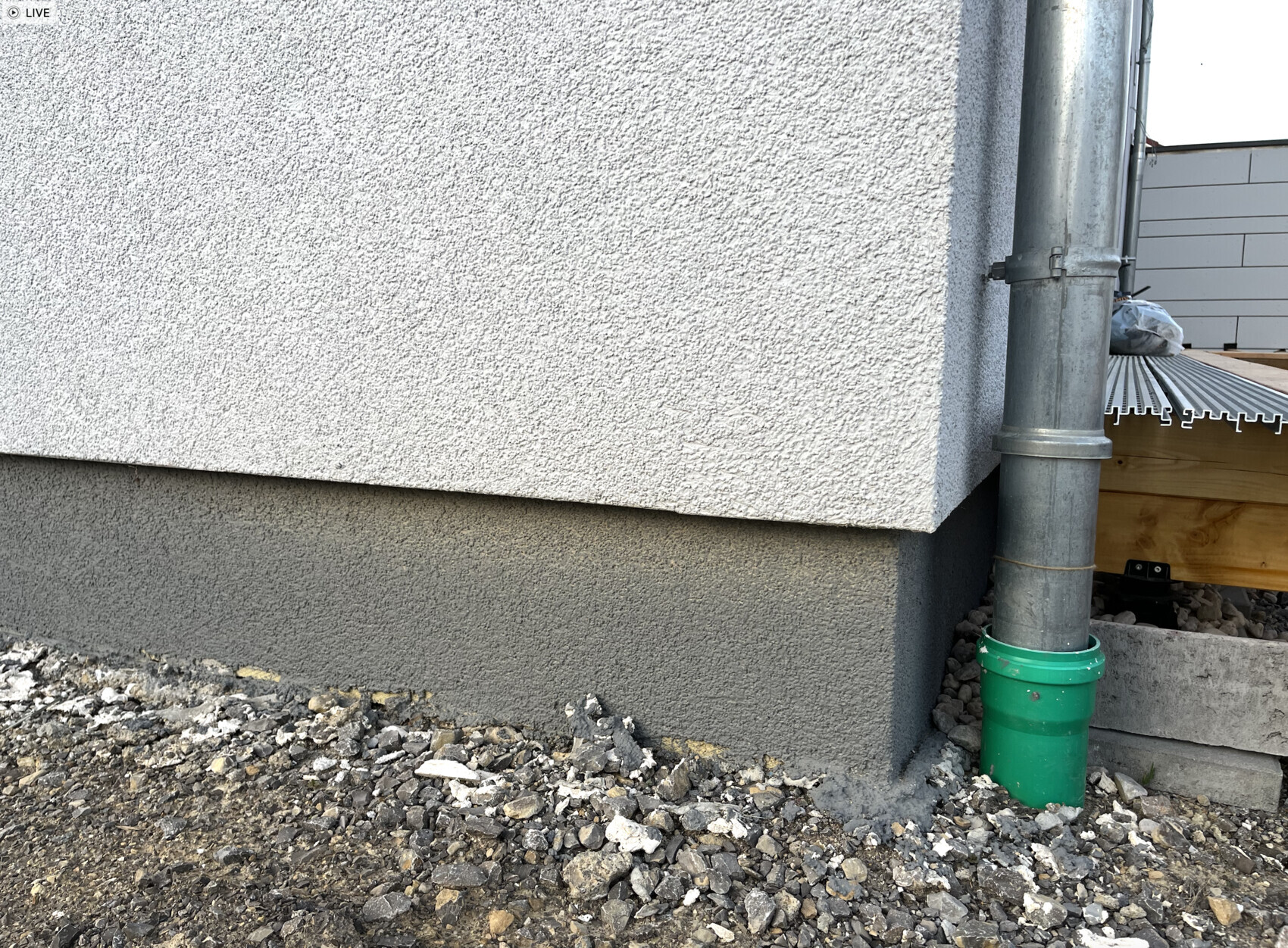 Exterior wall with rough plaster facade, dark foundation wall and vertical downpipe on the right
