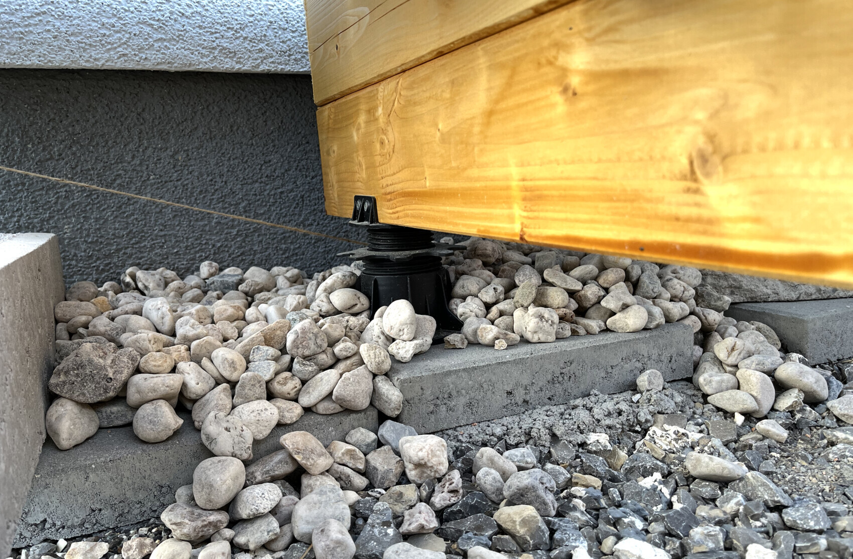Adjustable plastic foot under a wooden deck substructure on gravel