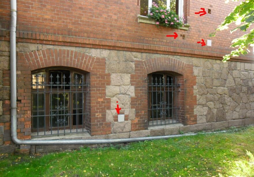 Exterior wall made of brick and natural stone, barred window; arrows mark inspection points