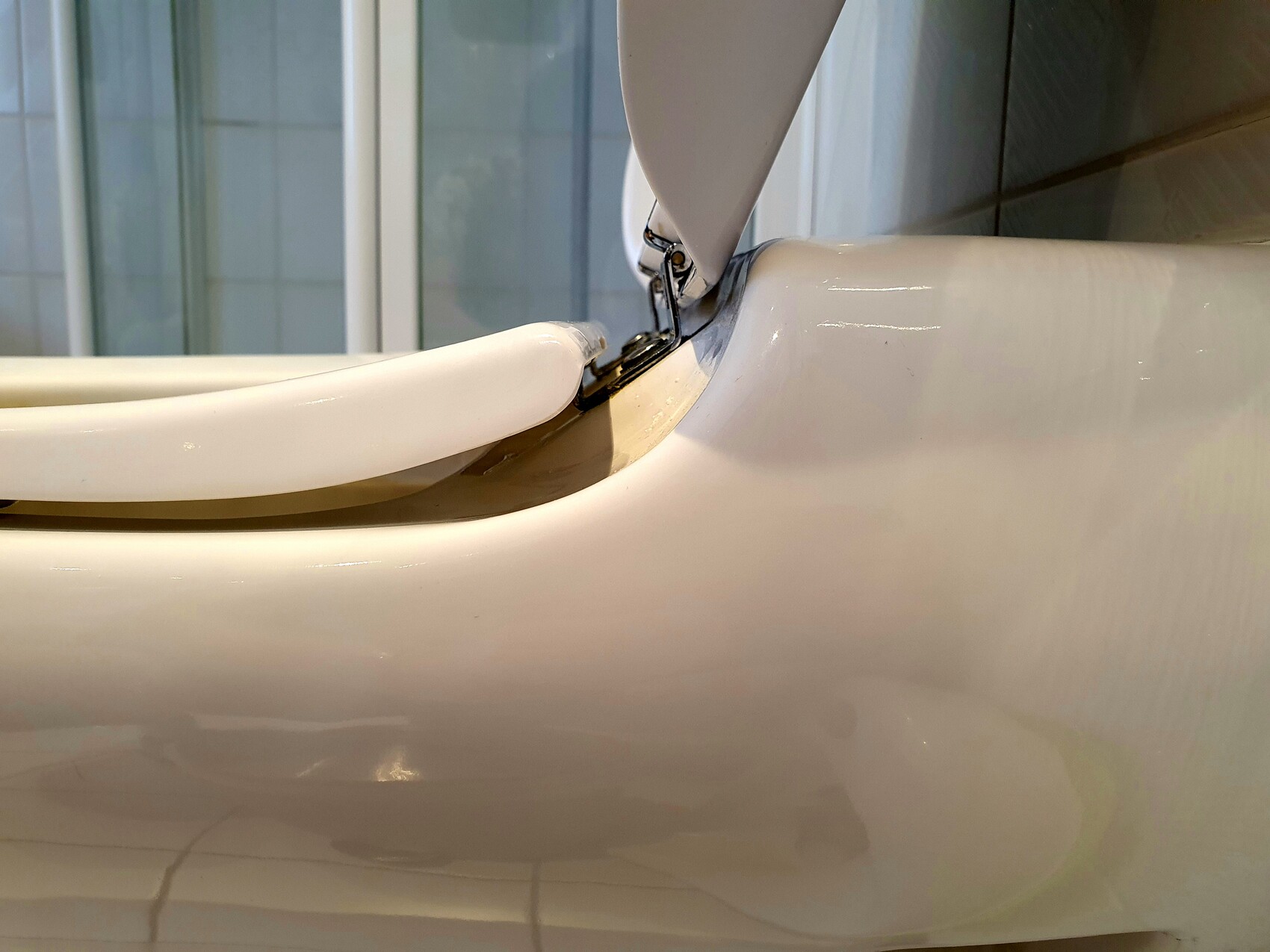 Close-up of a white toilet with open lid and metal hinge