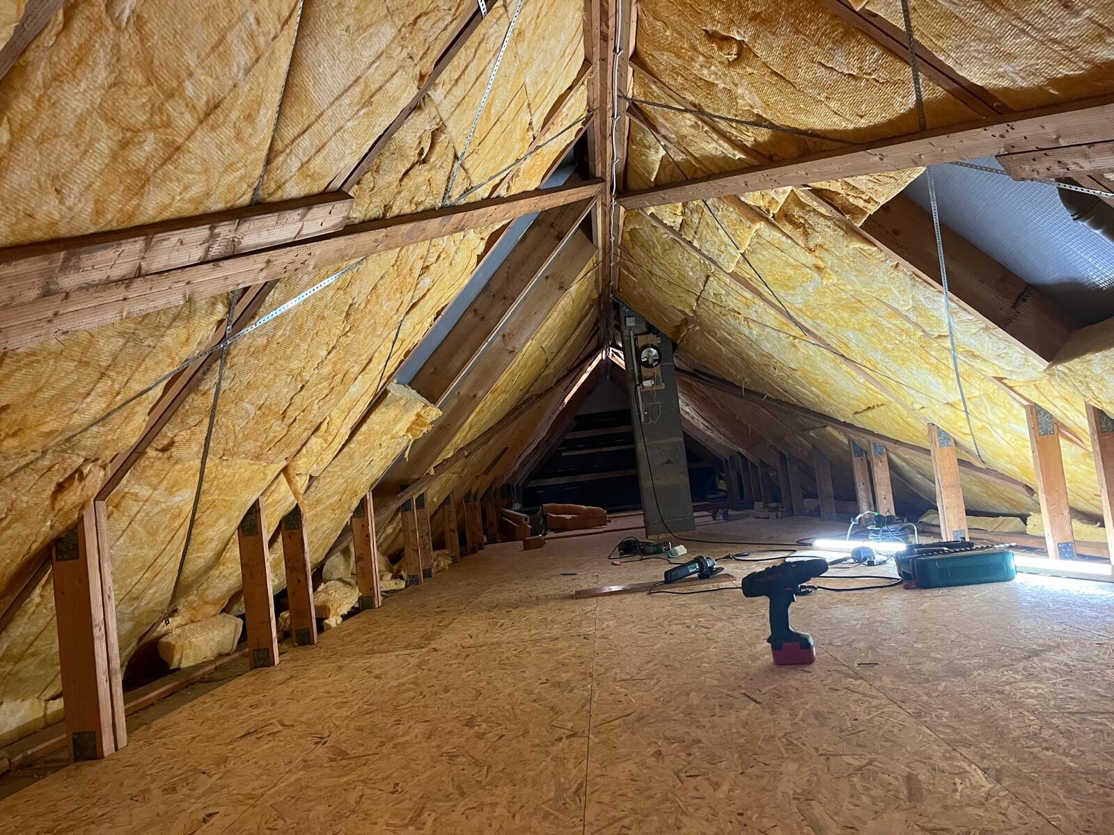 Dachboden mit Holzträgern, gelber Dämmstoff, Werkzeuge und Akku-Bohrmaschine