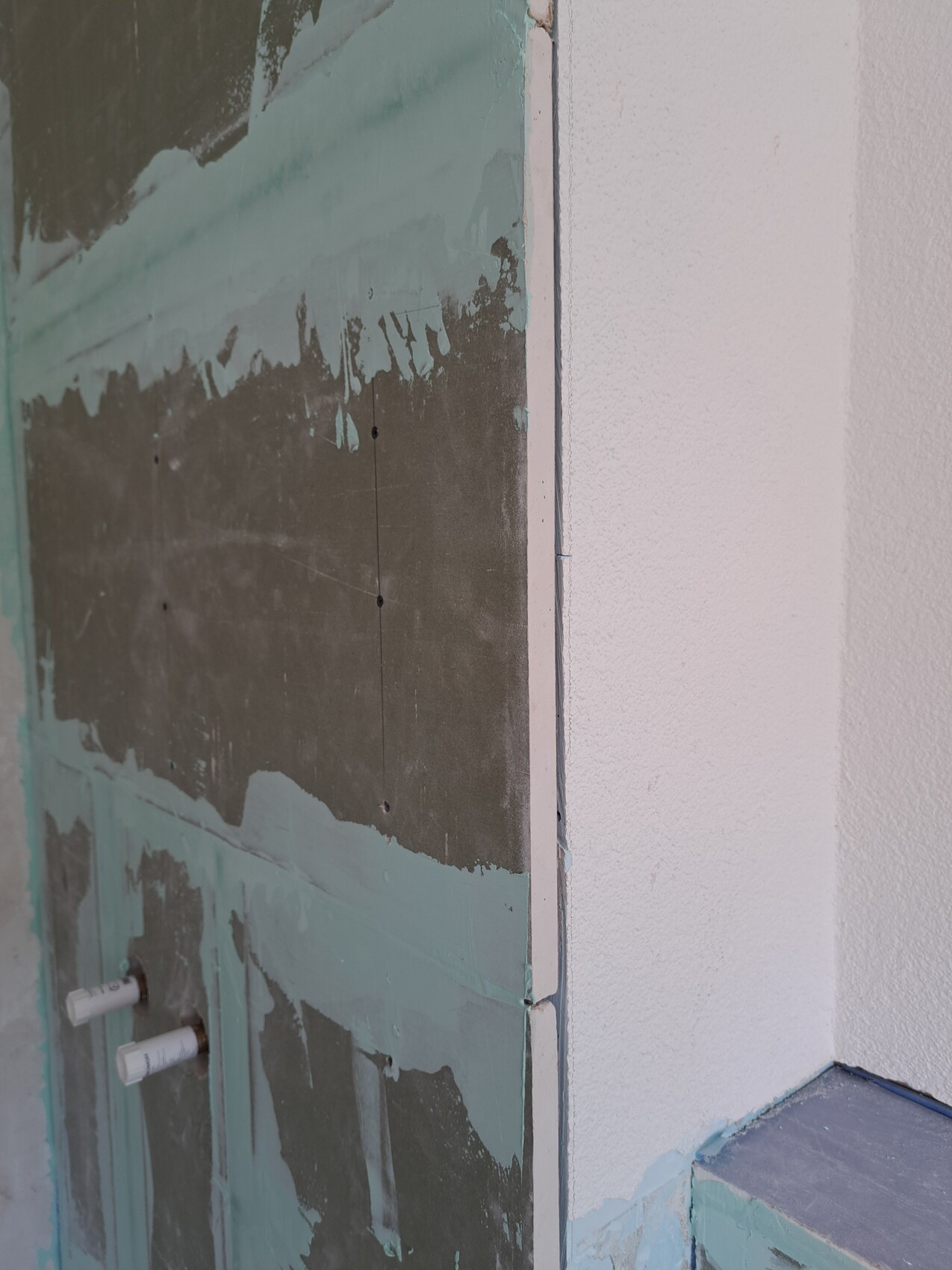 Construction site wall: green plasterboard ready for plastering, screw joints, two pipe connections at the bottom left.