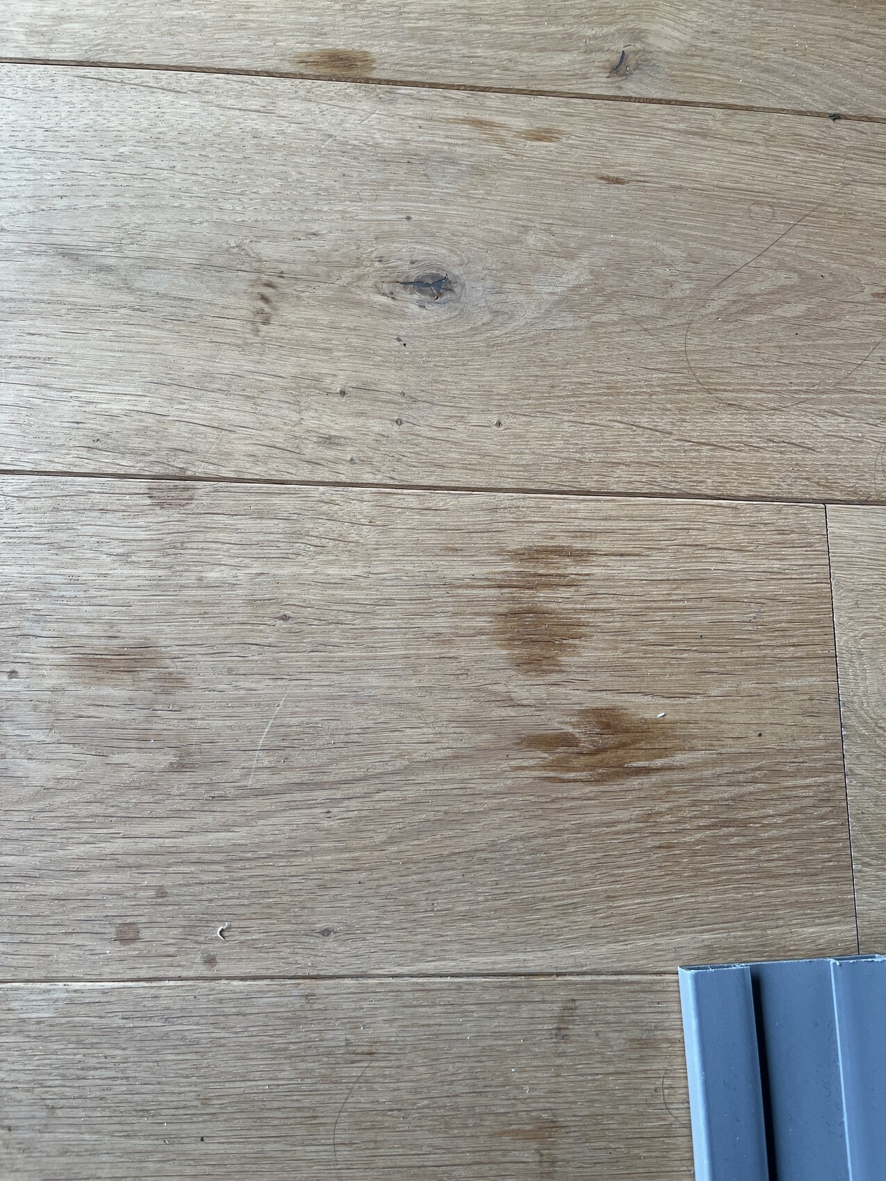 Wood floor with stains; a gray metal part visible at the lower right.