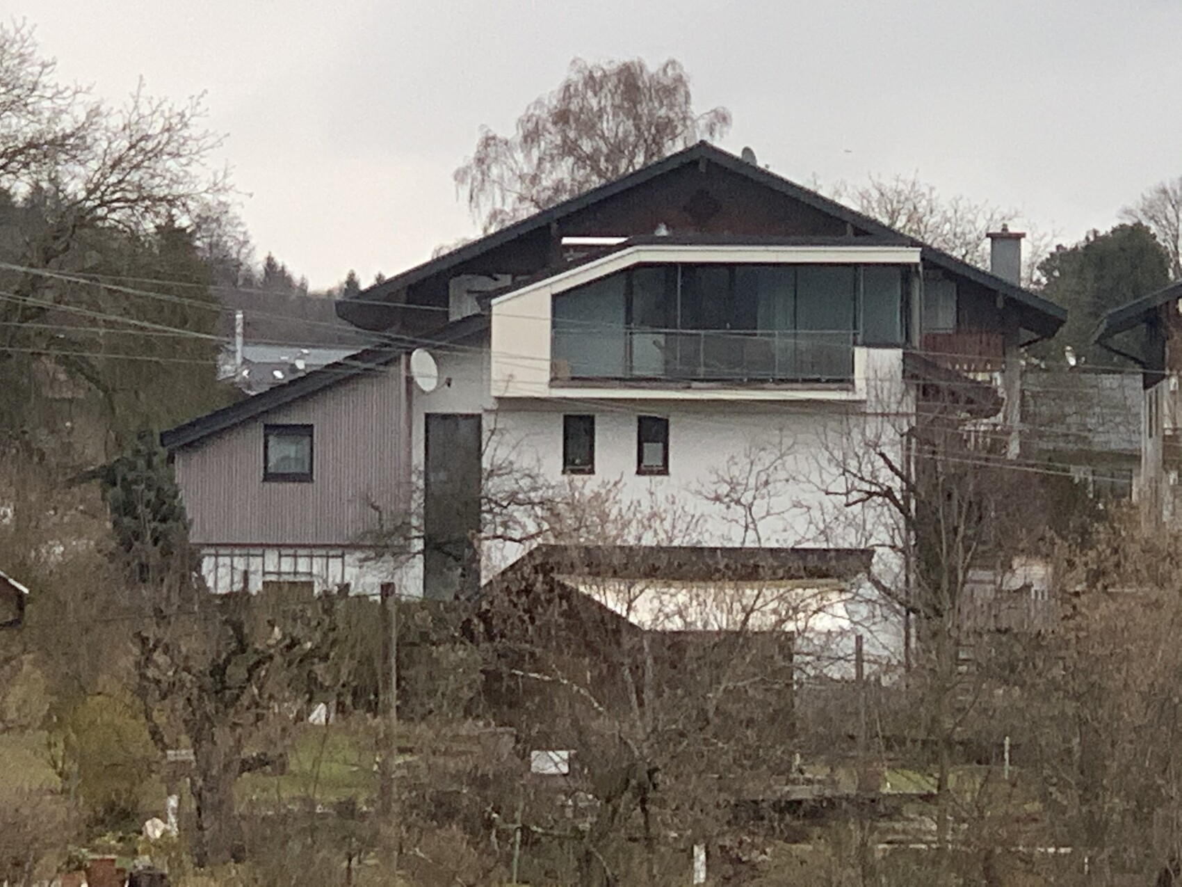 Two-story house with glass balustrade on the upper floor, bare trees in the garden in front