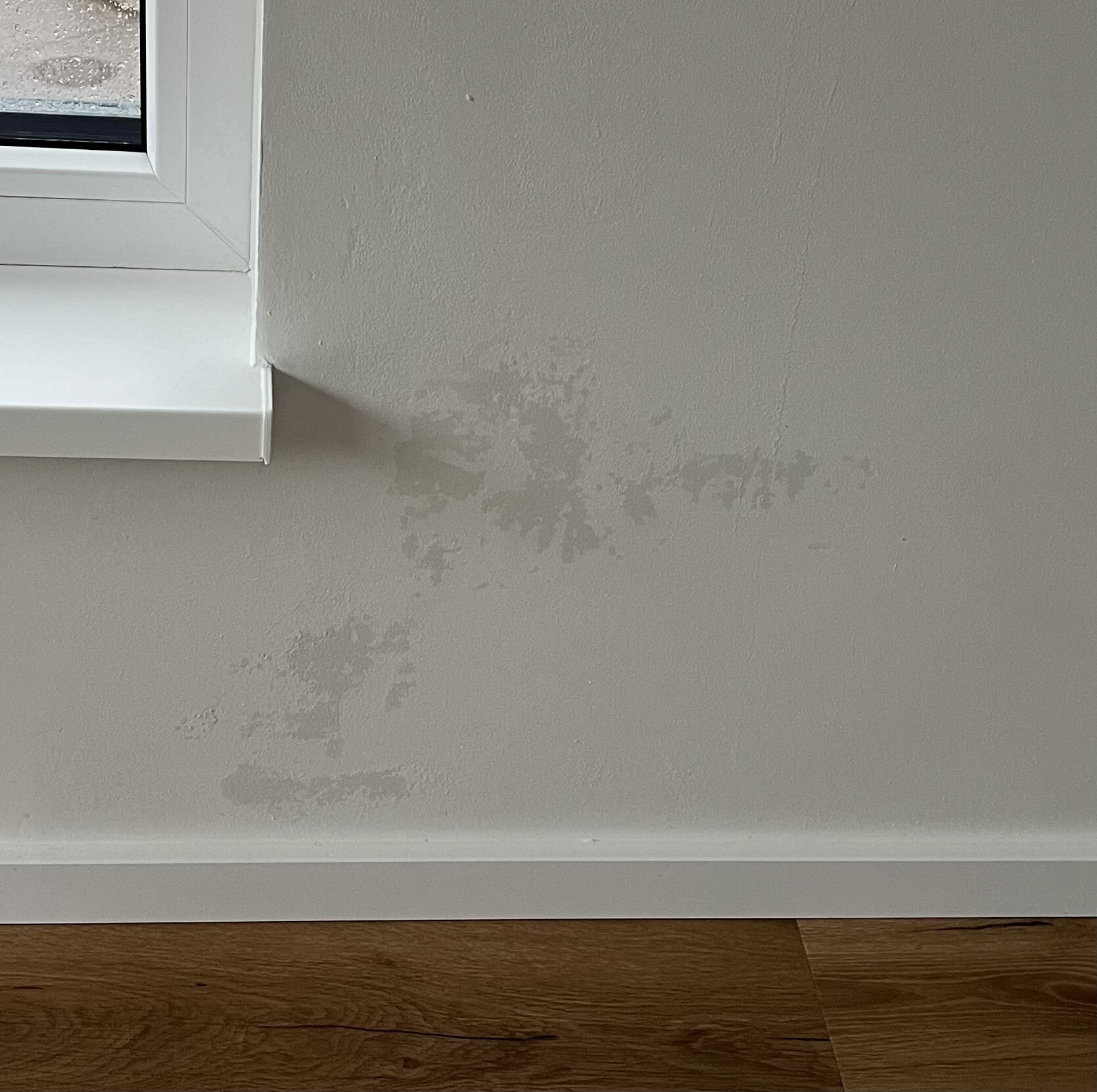 Wall with moisture damage, gray spots below window and baseboard.