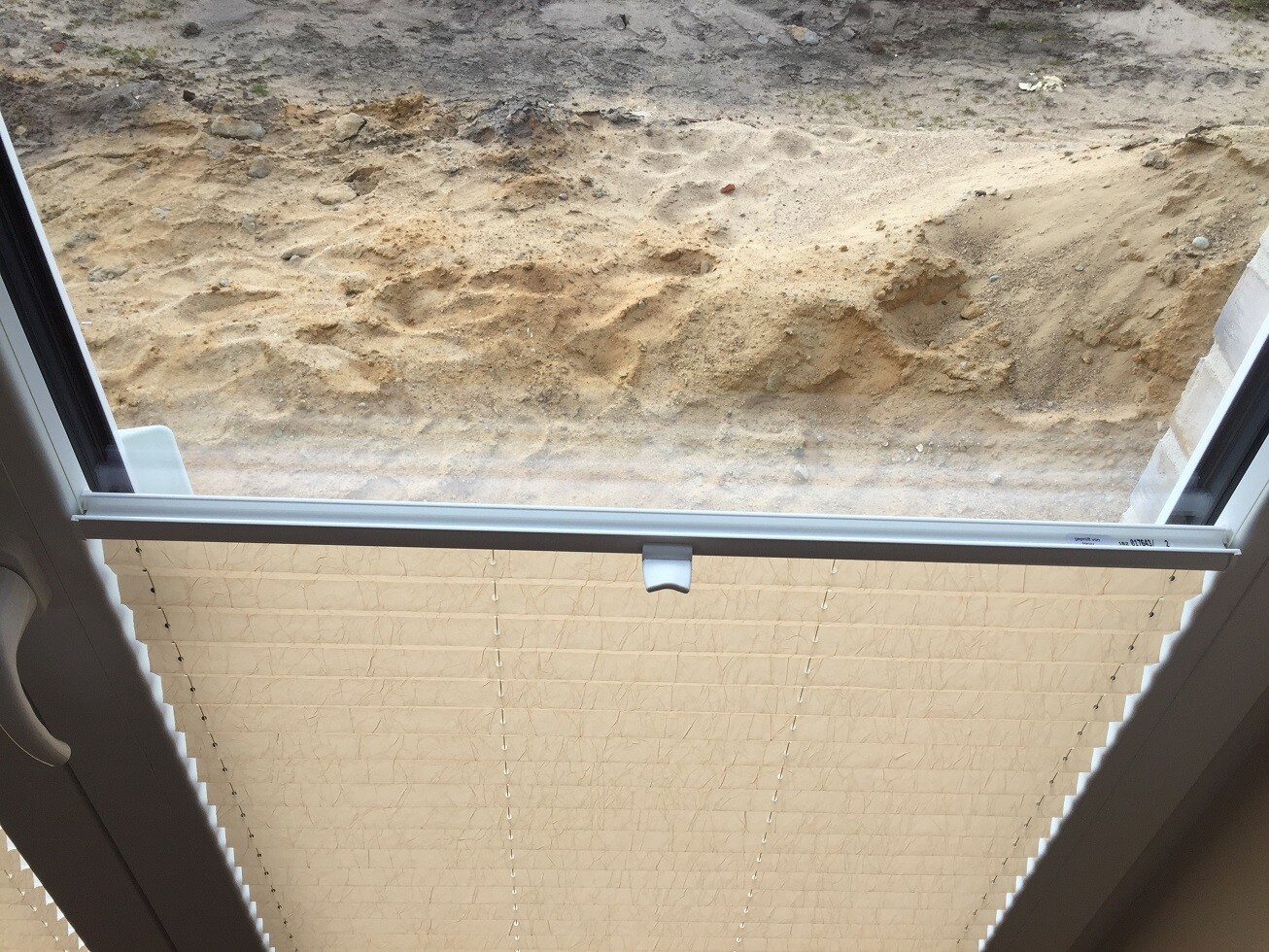 View from inside through the window with blinds onto sand and soil of a construction site