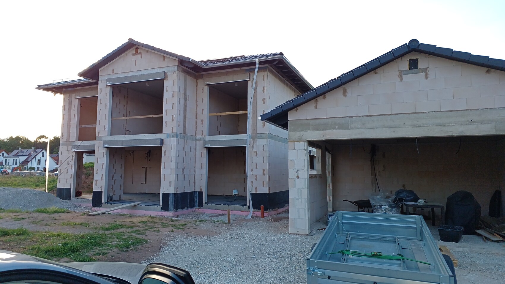 New build shell: Two-story house made of blocks, open spaces; construction equipment on site.