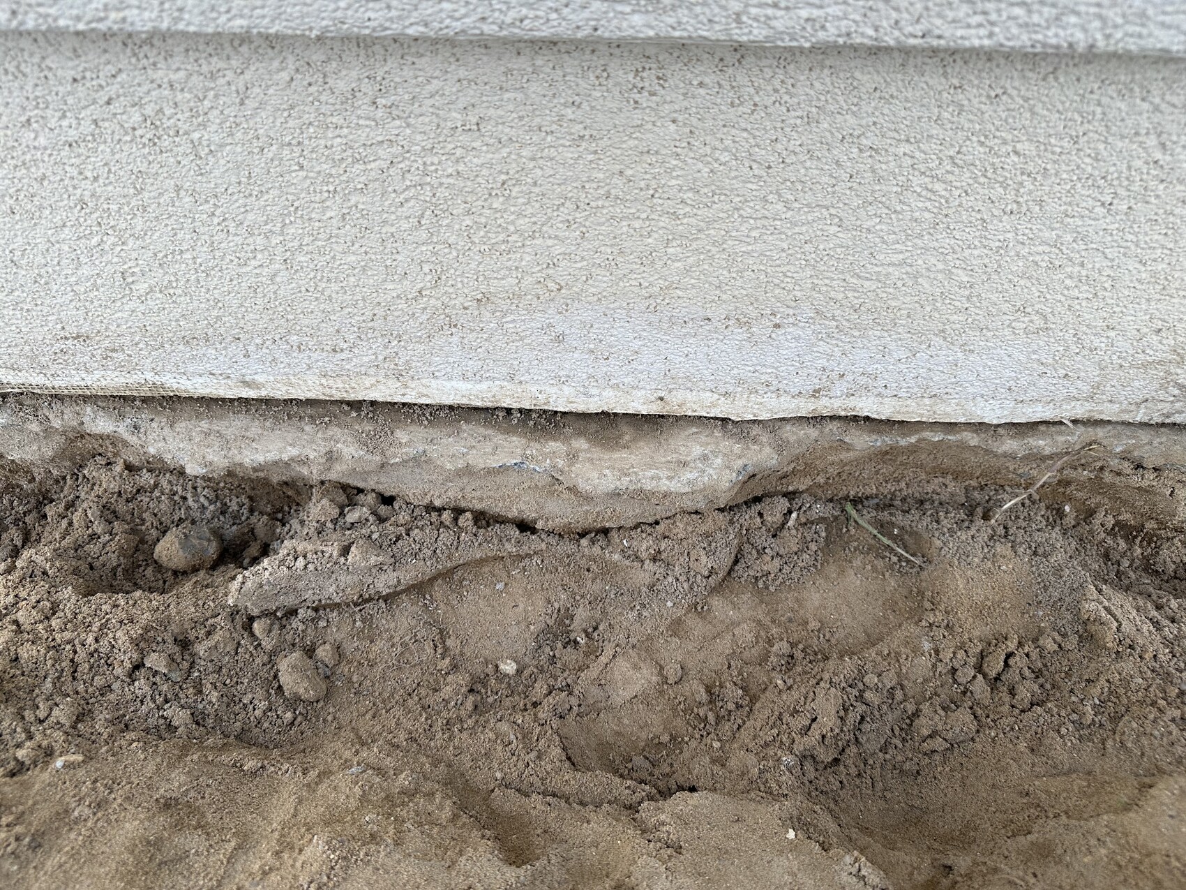 Bottom edge of a concrete wall above loose soil with excavation and stones.