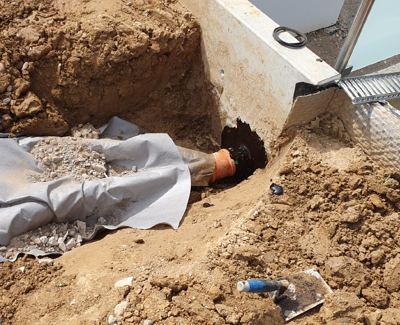 Open construction pit with orange pipe and concrete foundation at a building site.