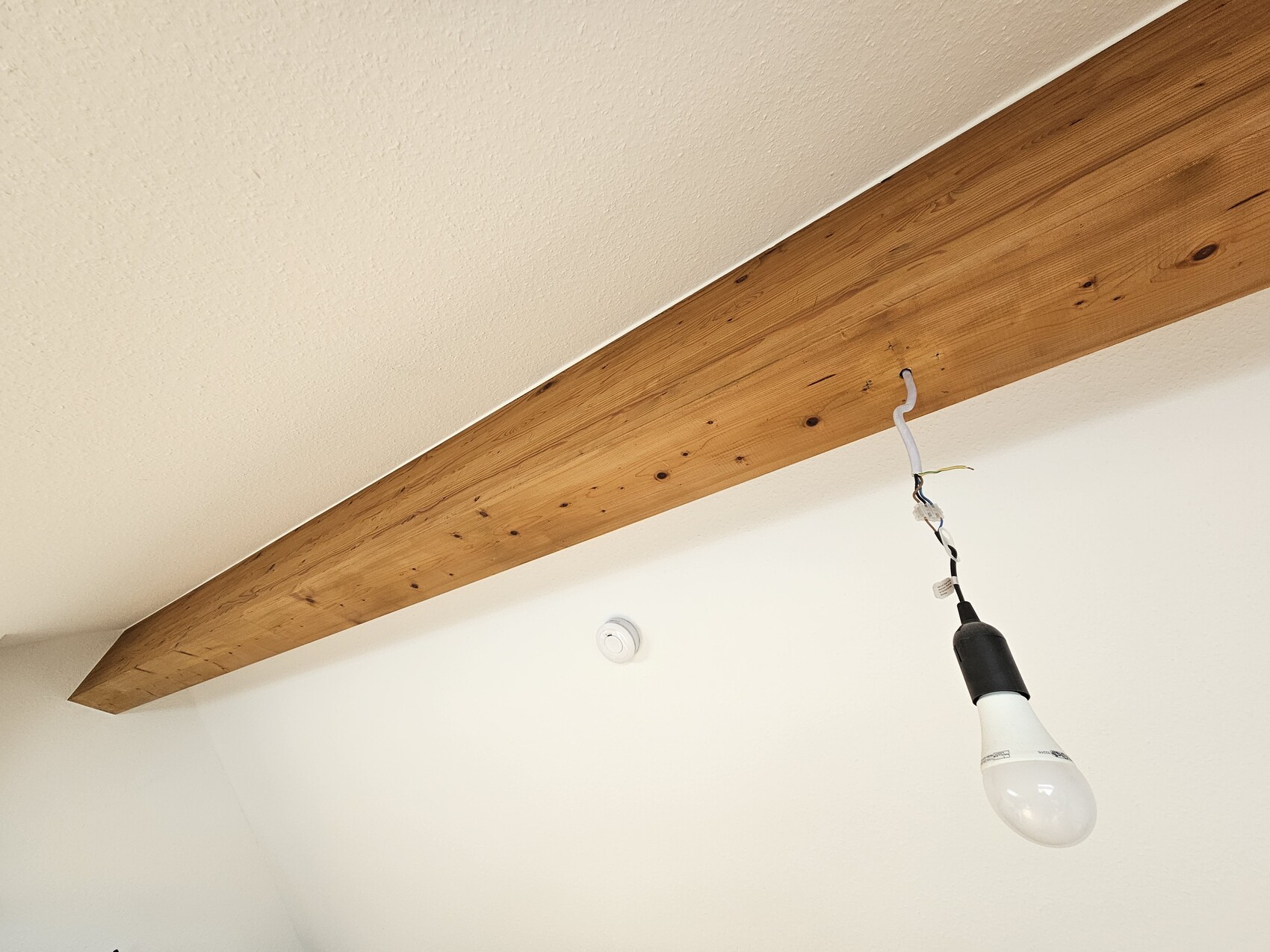 Hanging light bulb with exposed cables under a wooden beam on the ceiling.