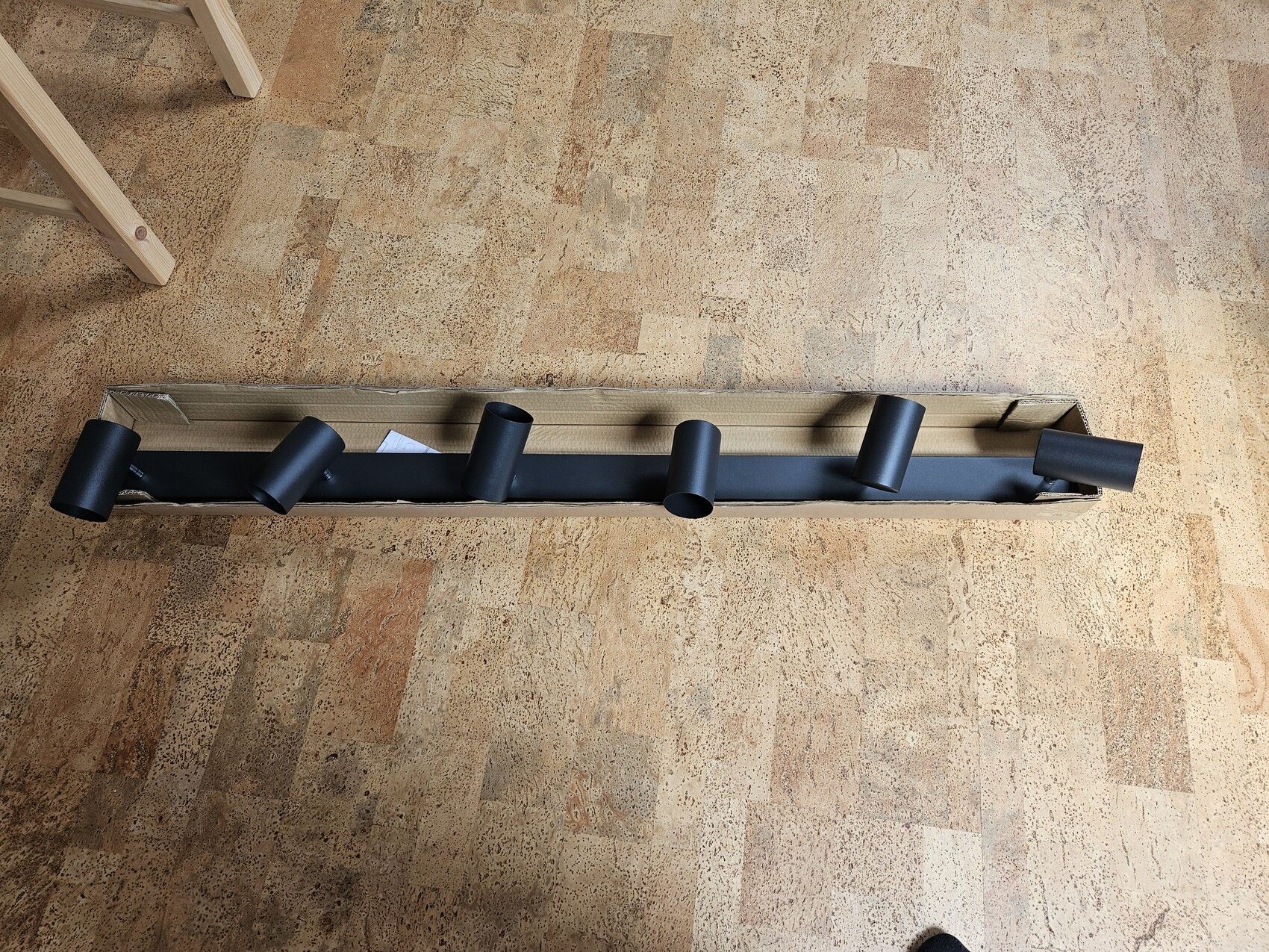 Black light bar with five spotlights in a cardboard box on wooden floor.