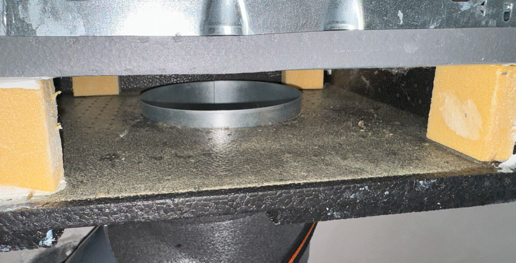 Round metal ring rests on a rough black surface, framed by yellow-orange blocks.