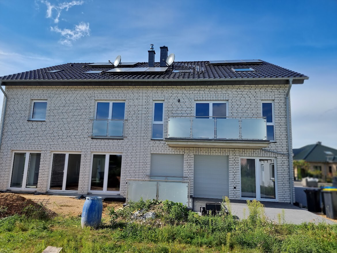 Two-story white brick house with balcony, roof solar panels, and satellite dishes.