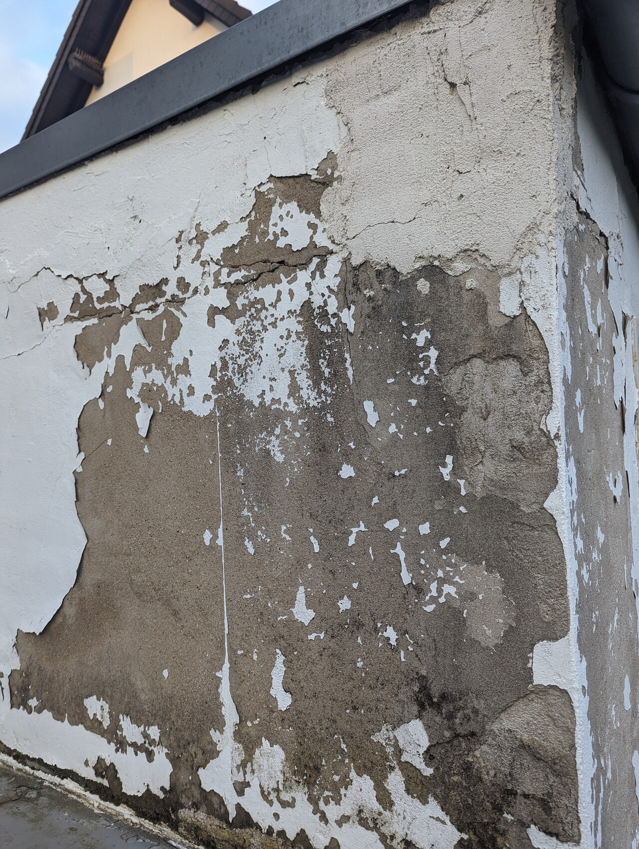 Exterior wall with peeling white paint; brown plaster and moisture underneath.