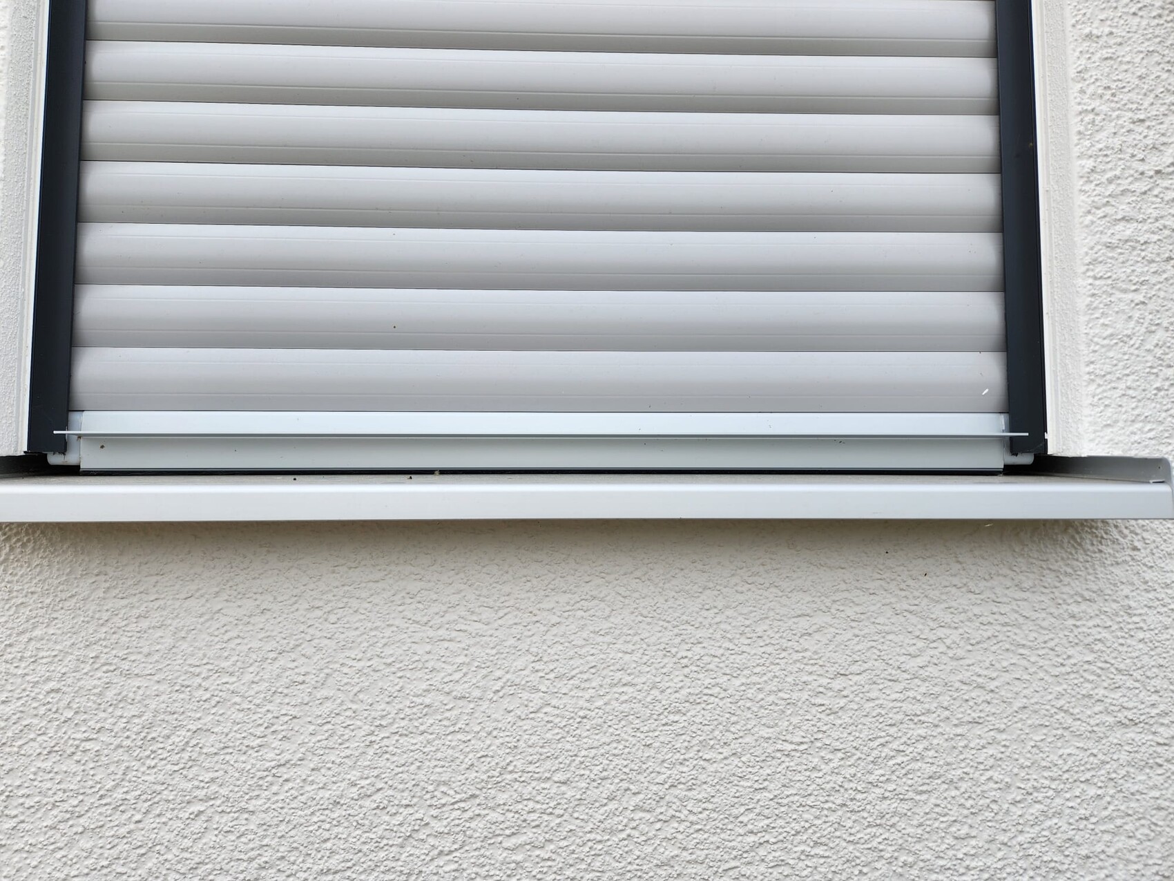 Closed roller shutter in front of the window, on a light rough wall.