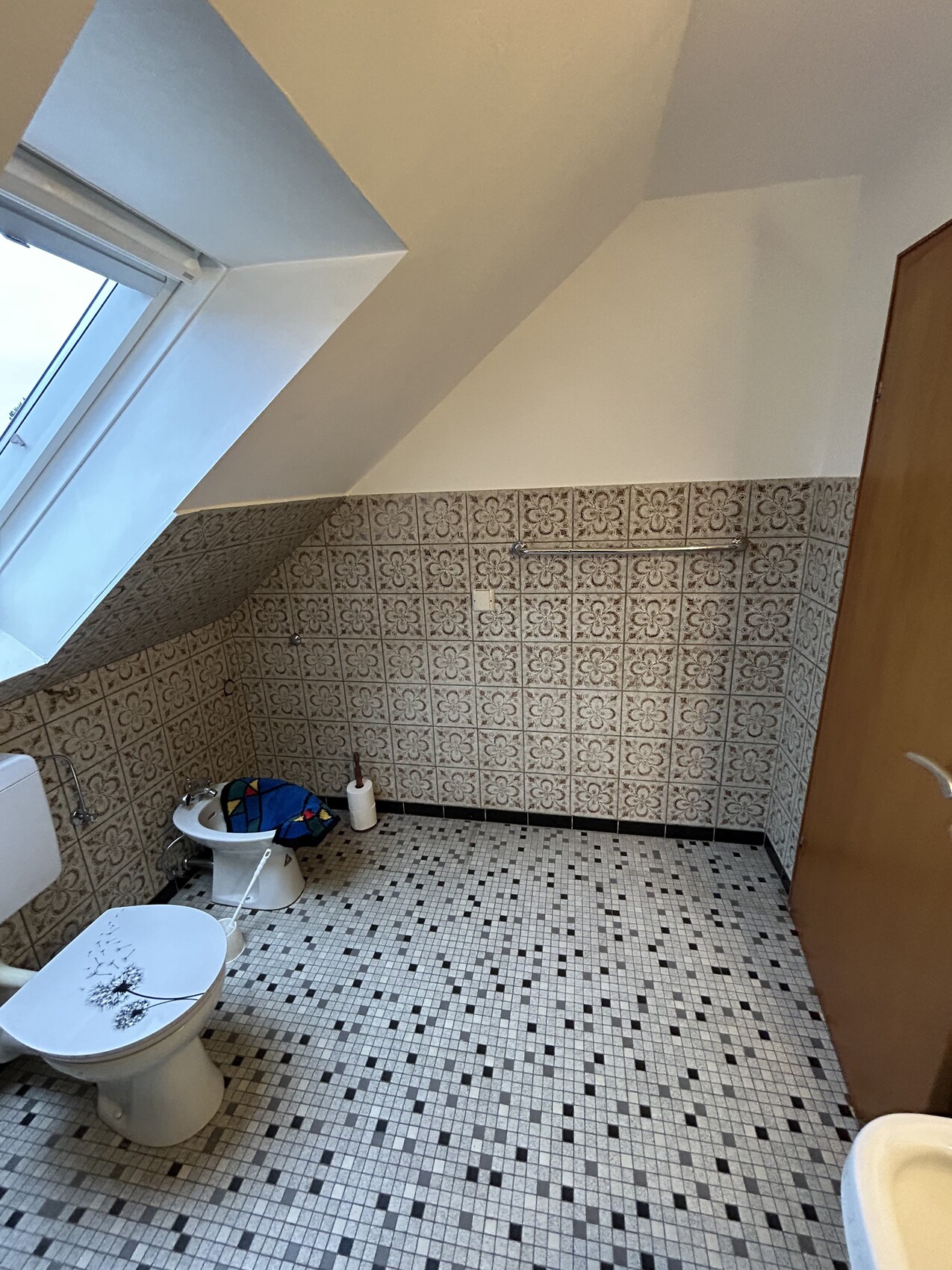 Dachgeschoss-Badezimmer mit Toilette, Bidet, Dachfenster und Musterfliesen.