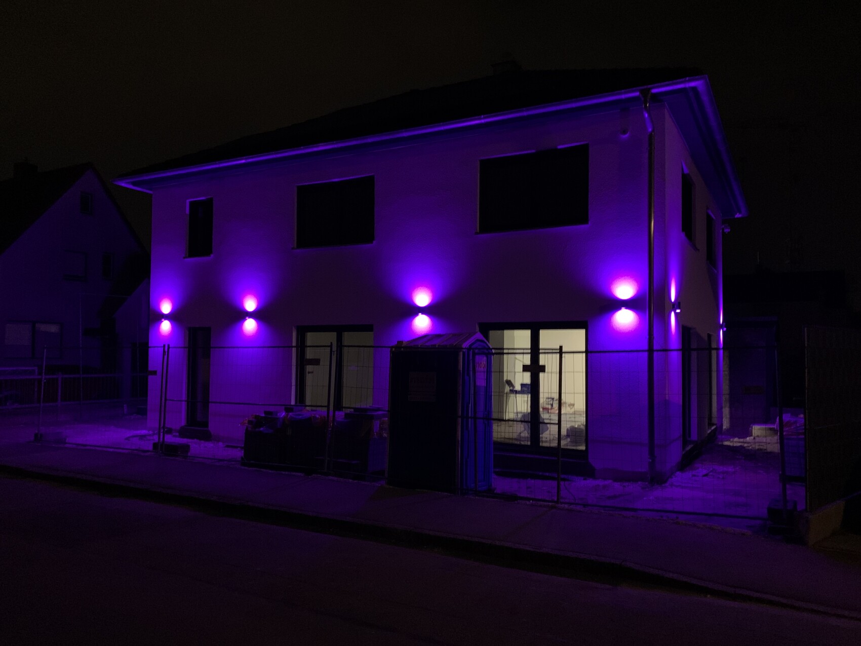 House at night with violet exterior lights on the facade and construction fence