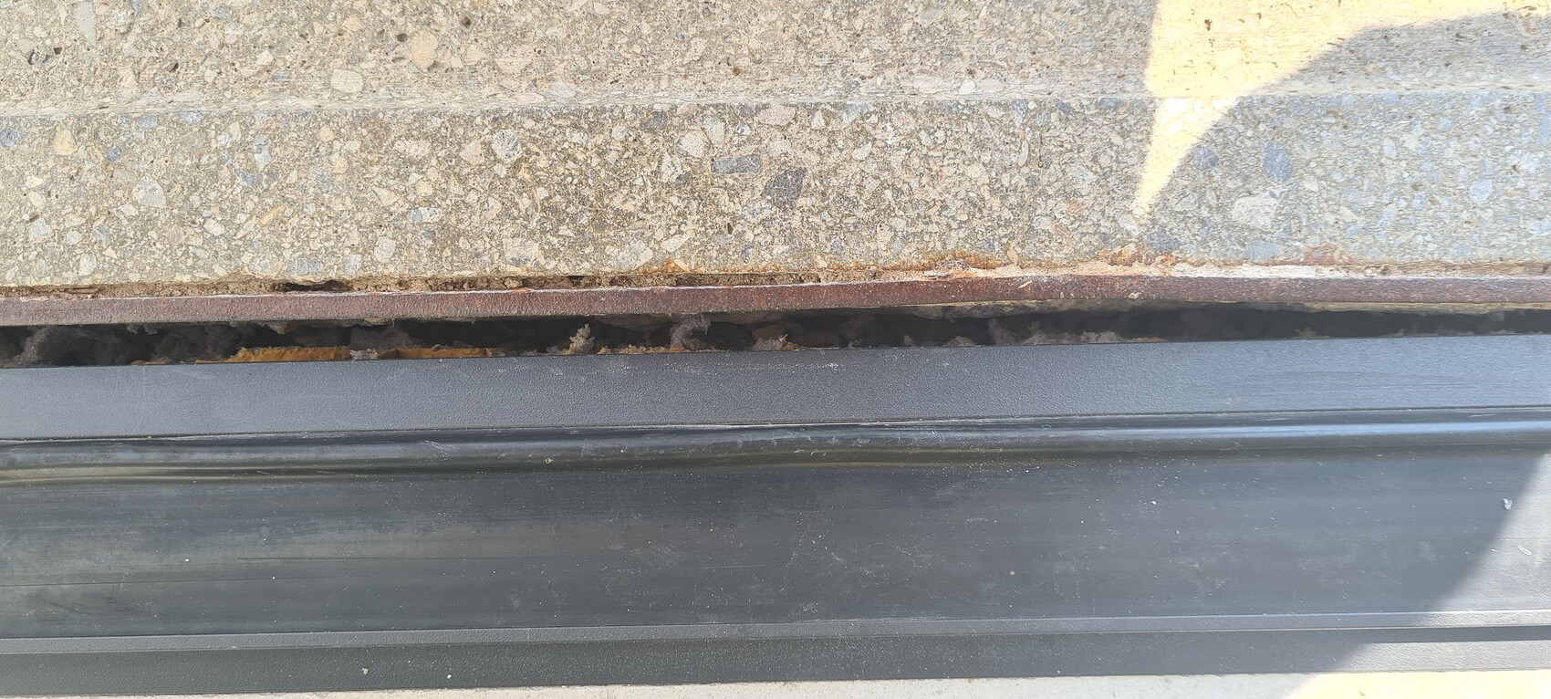 Visible concrete step with rusty edge, dark joint underneath, and black door threshold.