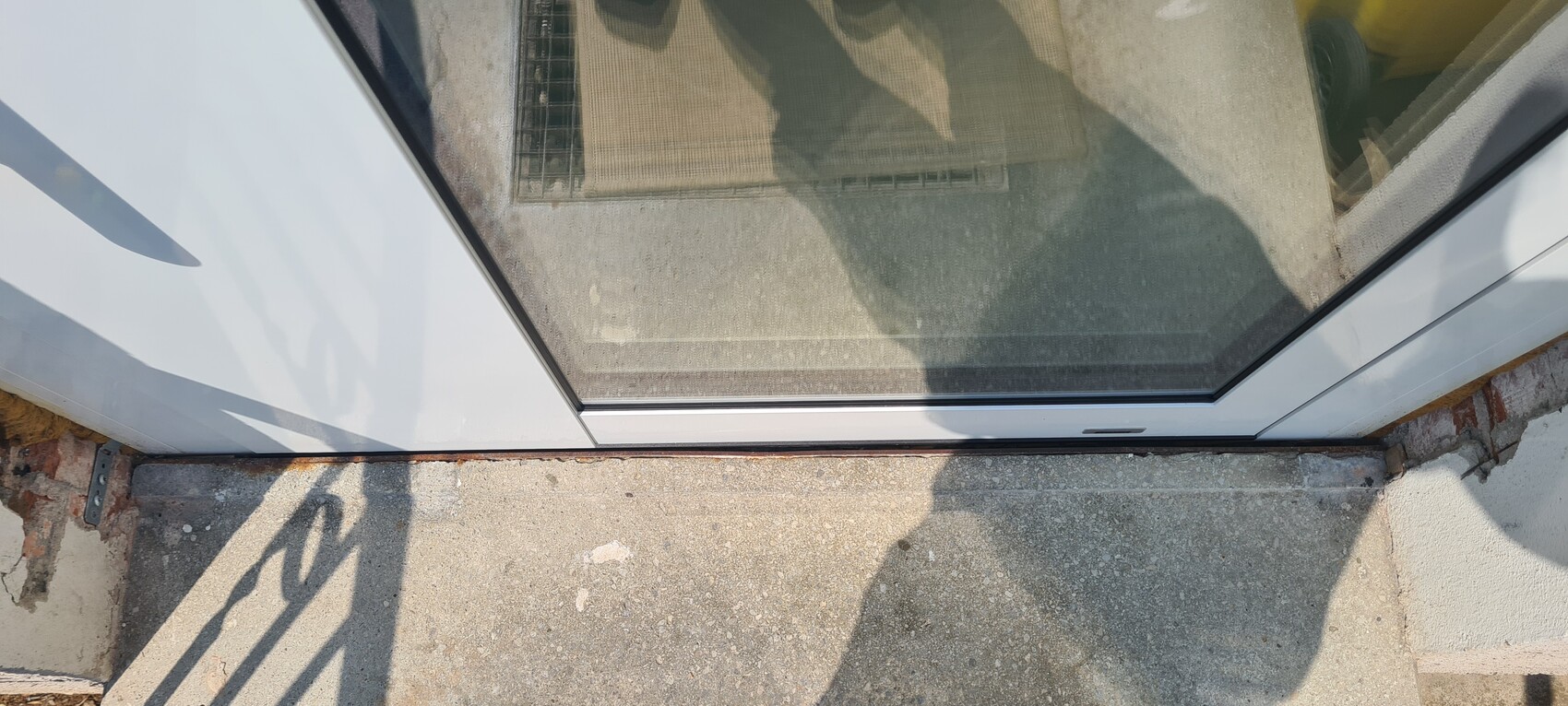 View through a glass sliding door onto the entrance step; shadow of a person on the concrete floor.