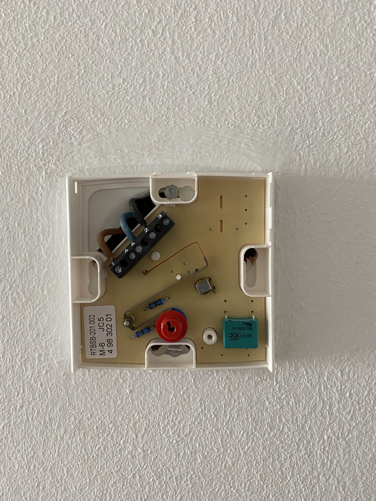 Inside view of a wall thermostat with circuit board, wires, resistors, and button