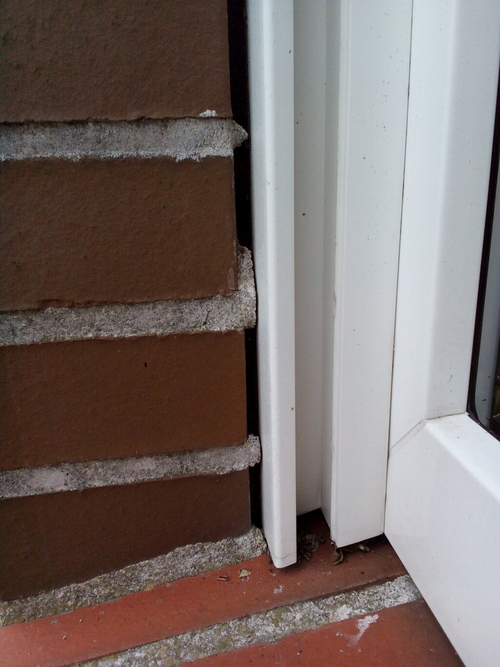 Red brick wall on the left next to a white door frame, door threshold with dust particles.