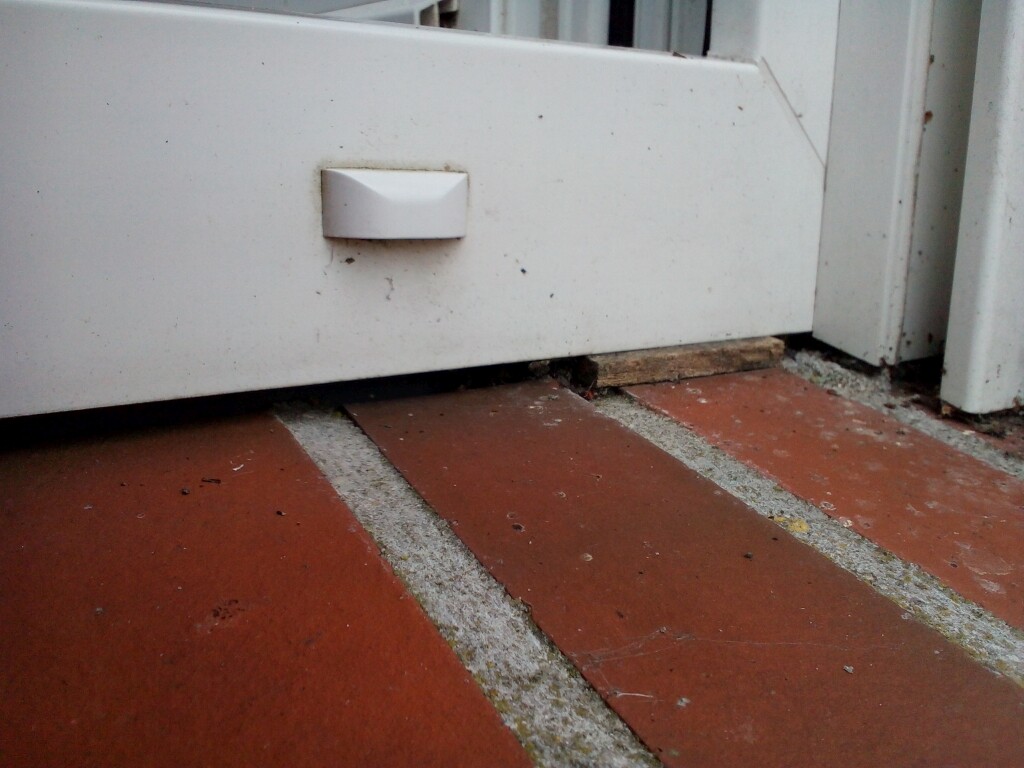 White metal casing with handle on red brick floor, wooden wedge underneath.