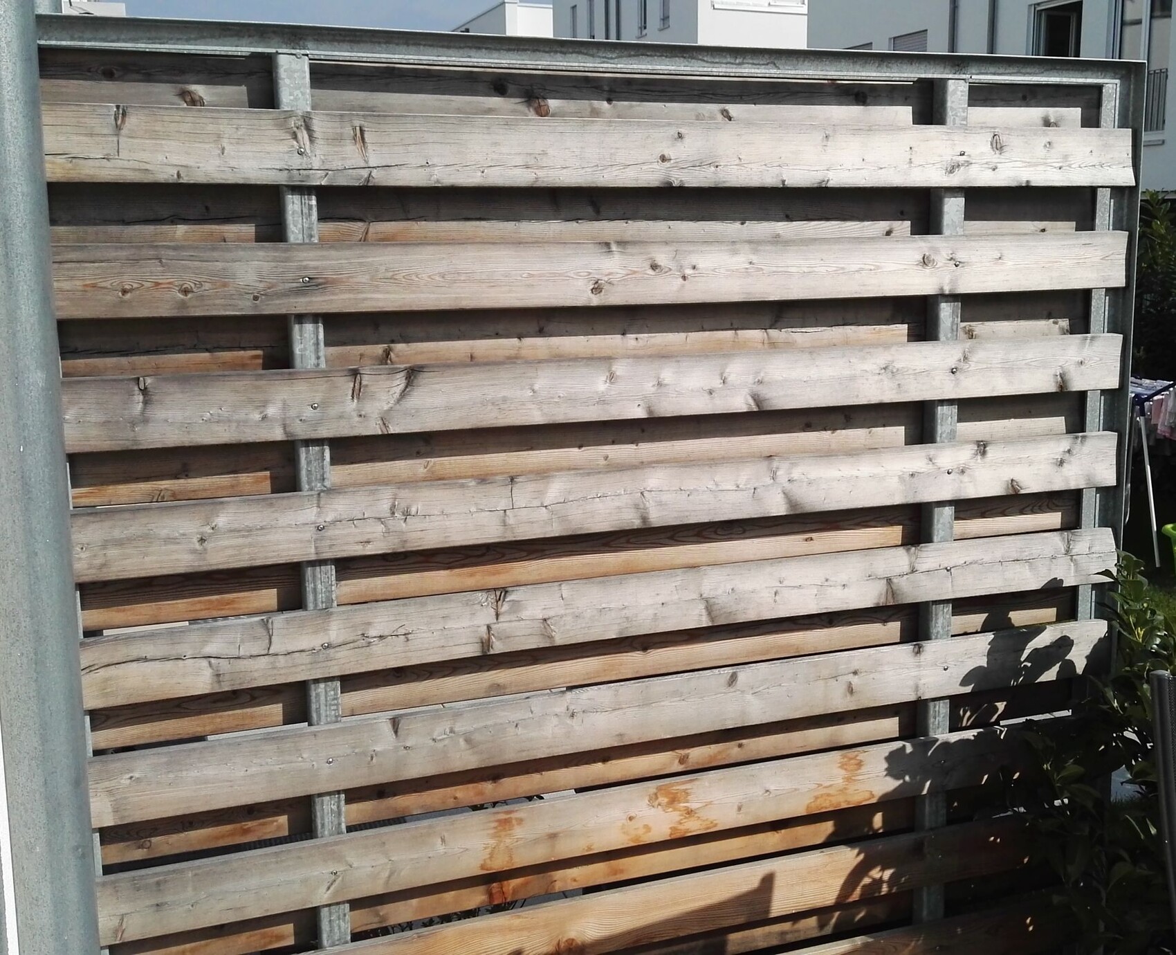 Holzlatten stapeln sich hinter einem Metallrahmen-Zaun, Holzsichtschutz im Garten.