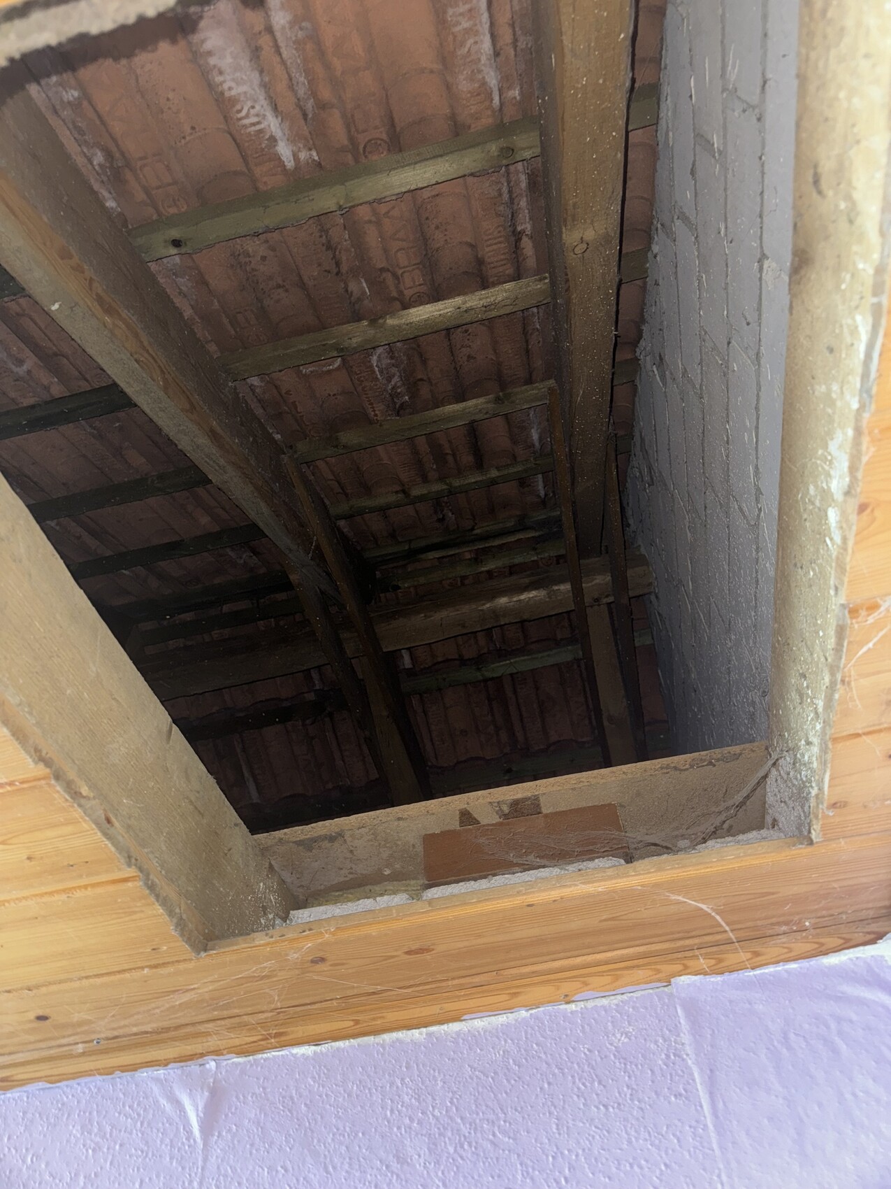 Open attic view with visible roof trusses, wooden beams, and tile ceiling.