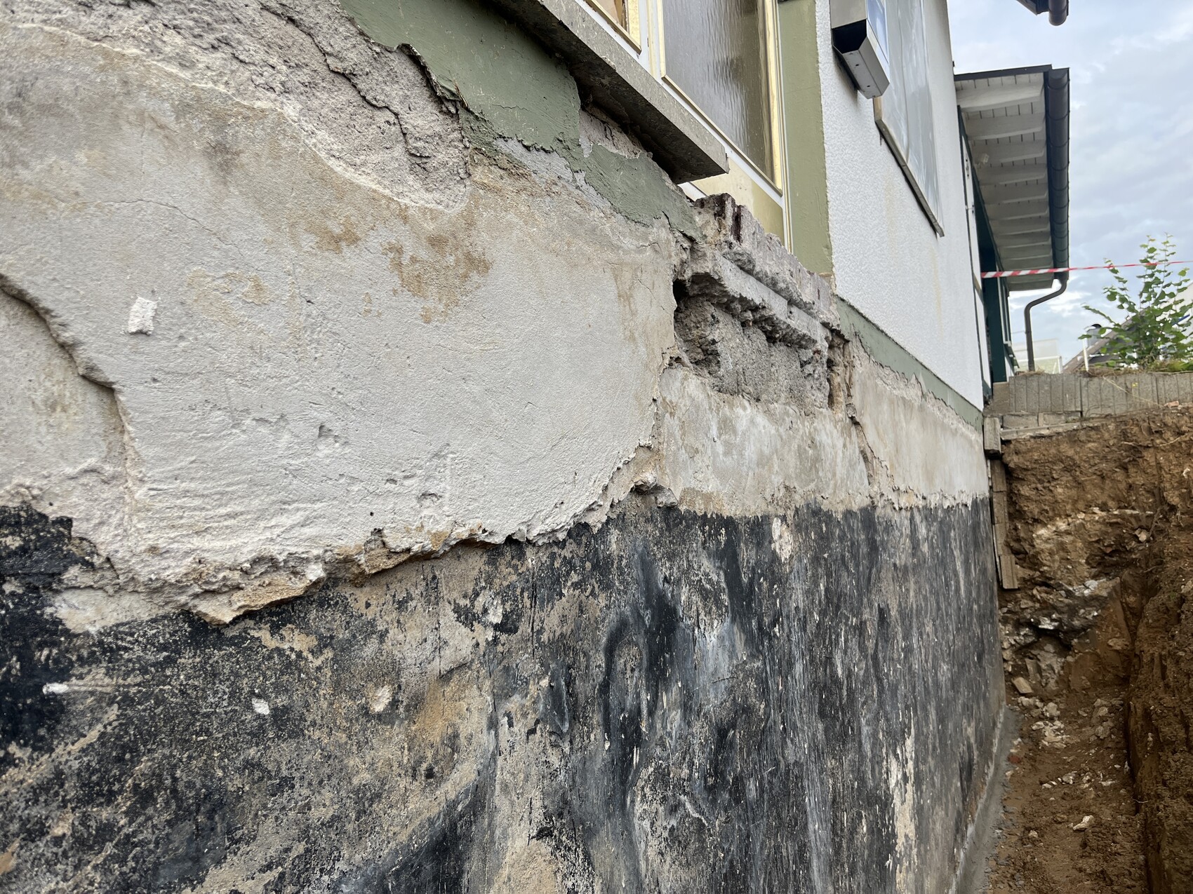 Exterior wall foundation with crumbling plaster and construction pit next to it.