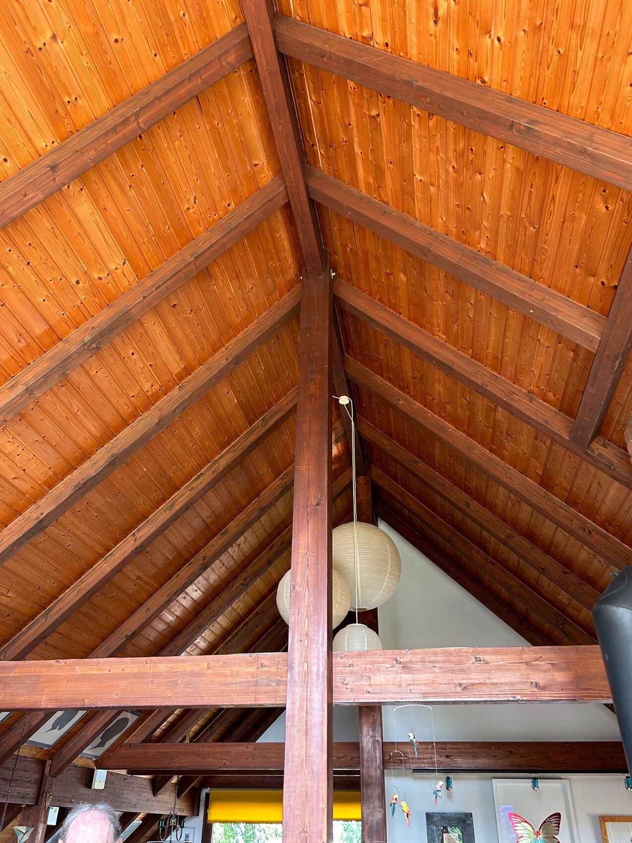 Interior view of an open wooden roof structure with visible beams and white paper lanterns.