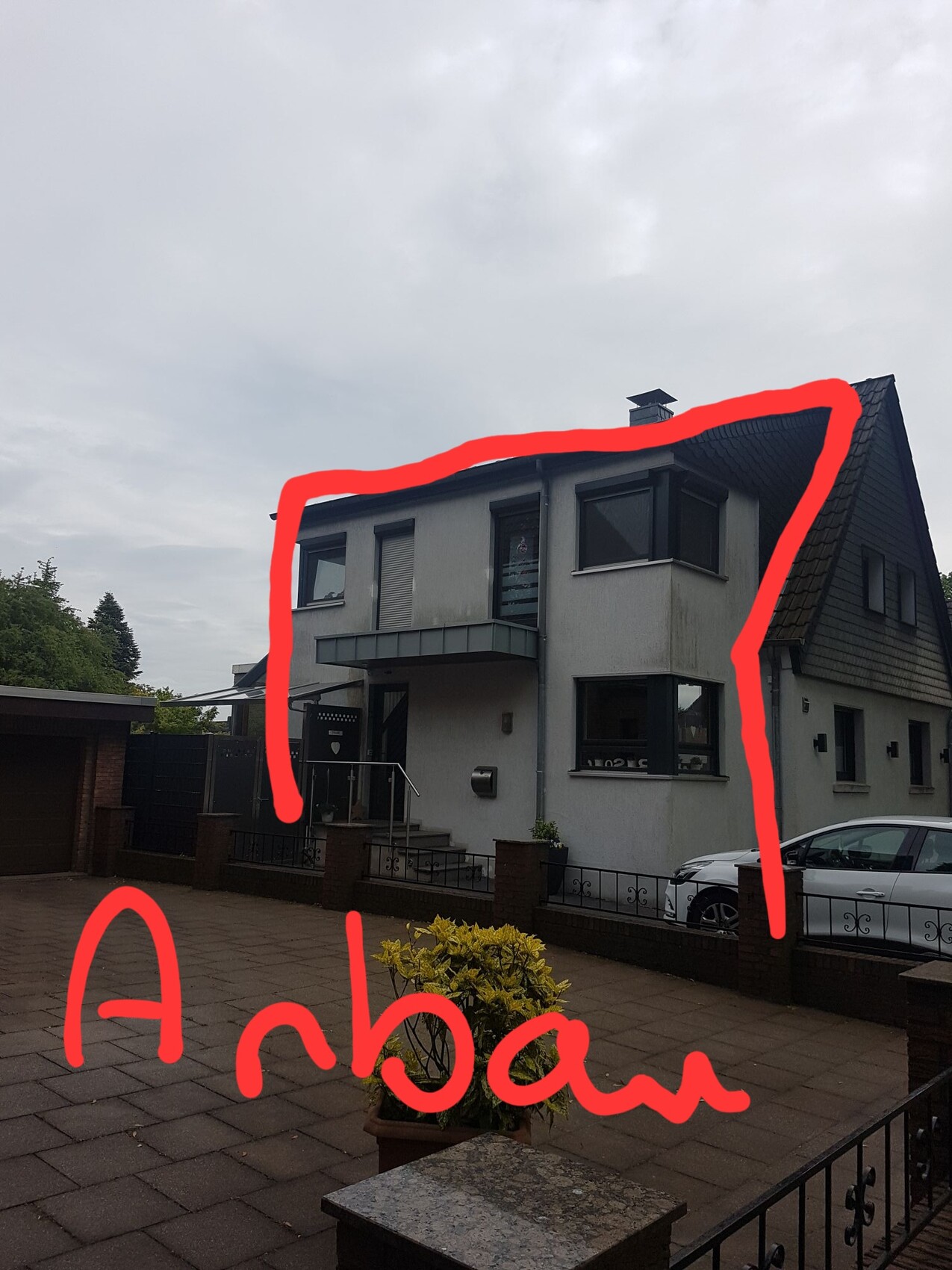 Zweistöckiges graues Haus mit großen Fenstern, Treppe zum Eingang, geparktes Auto rechts.