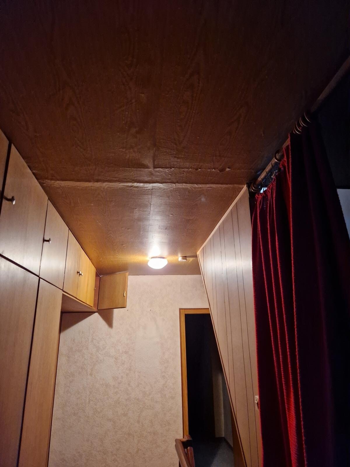 Narrow corridor with wooden panelling on the left, red curtains on the right, ceiling light in the center.