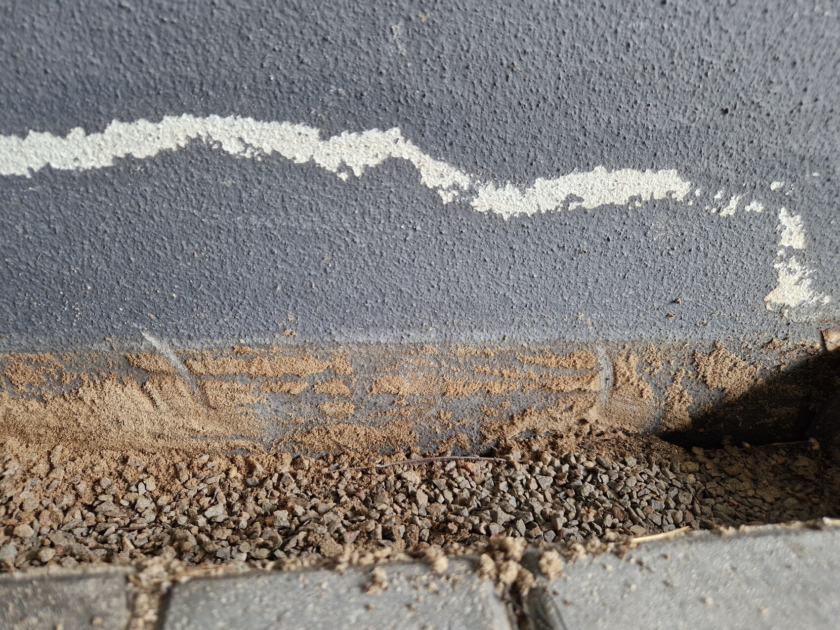 Gray concrete wall with white line; ground of gravel and sand.