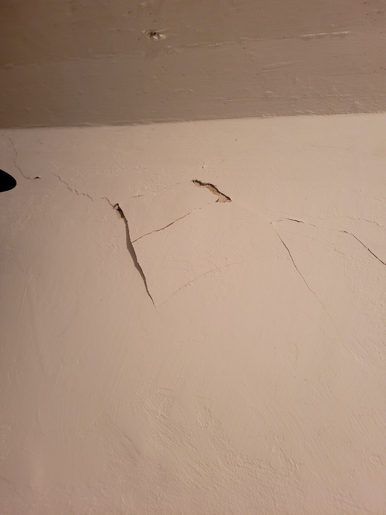 Beige wall with several fine cracks and crumbling plaster.