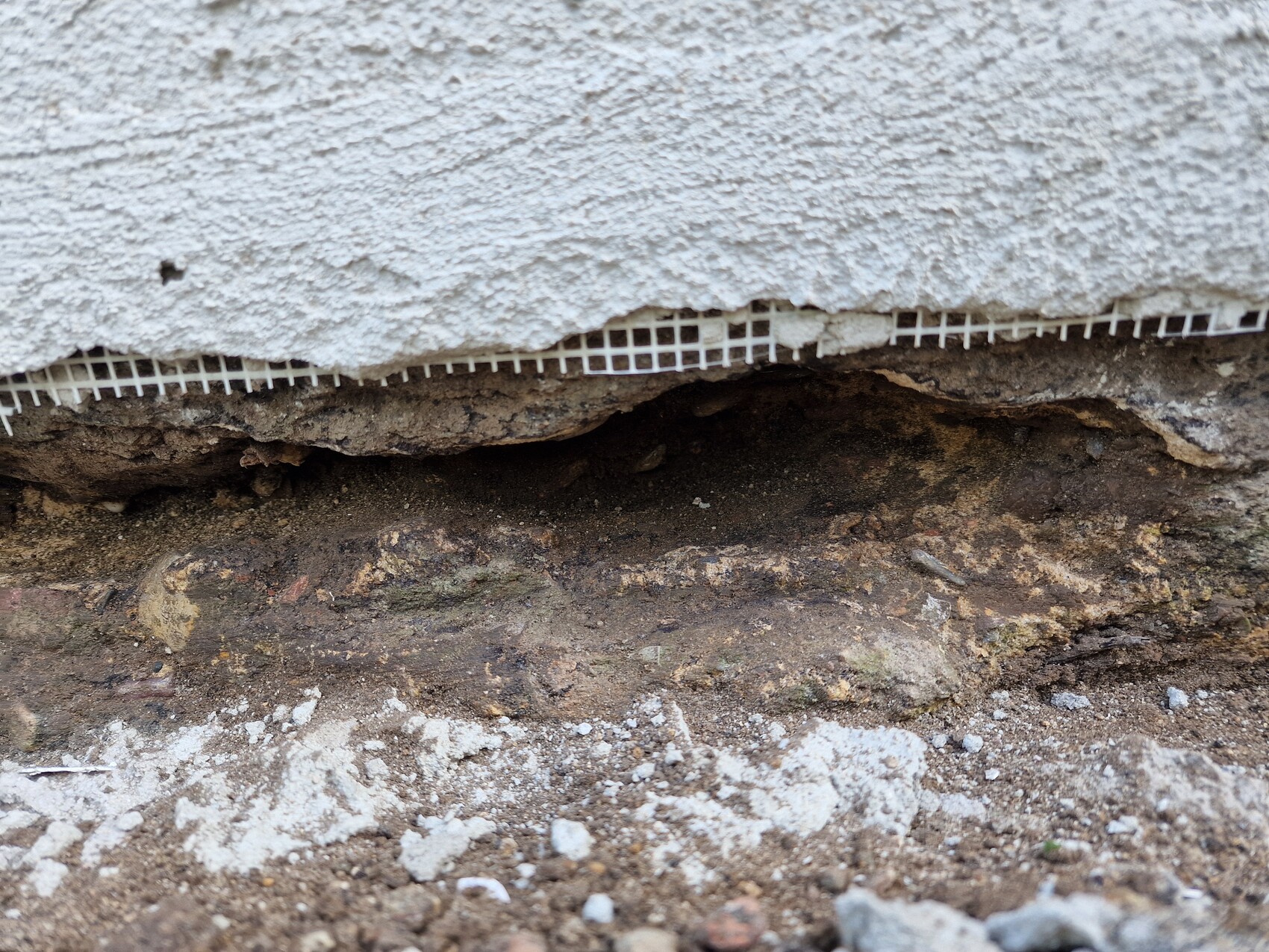 Underside of a plastered wall; exposed soil and crumbling plaster at the foundation.