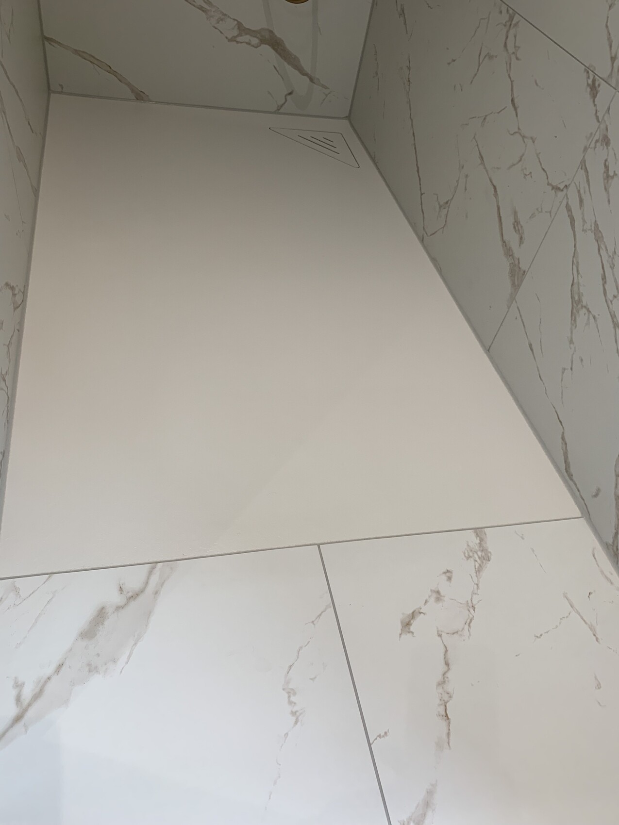 Corner shower with white marble-effect tiles; low white bench in the corner.