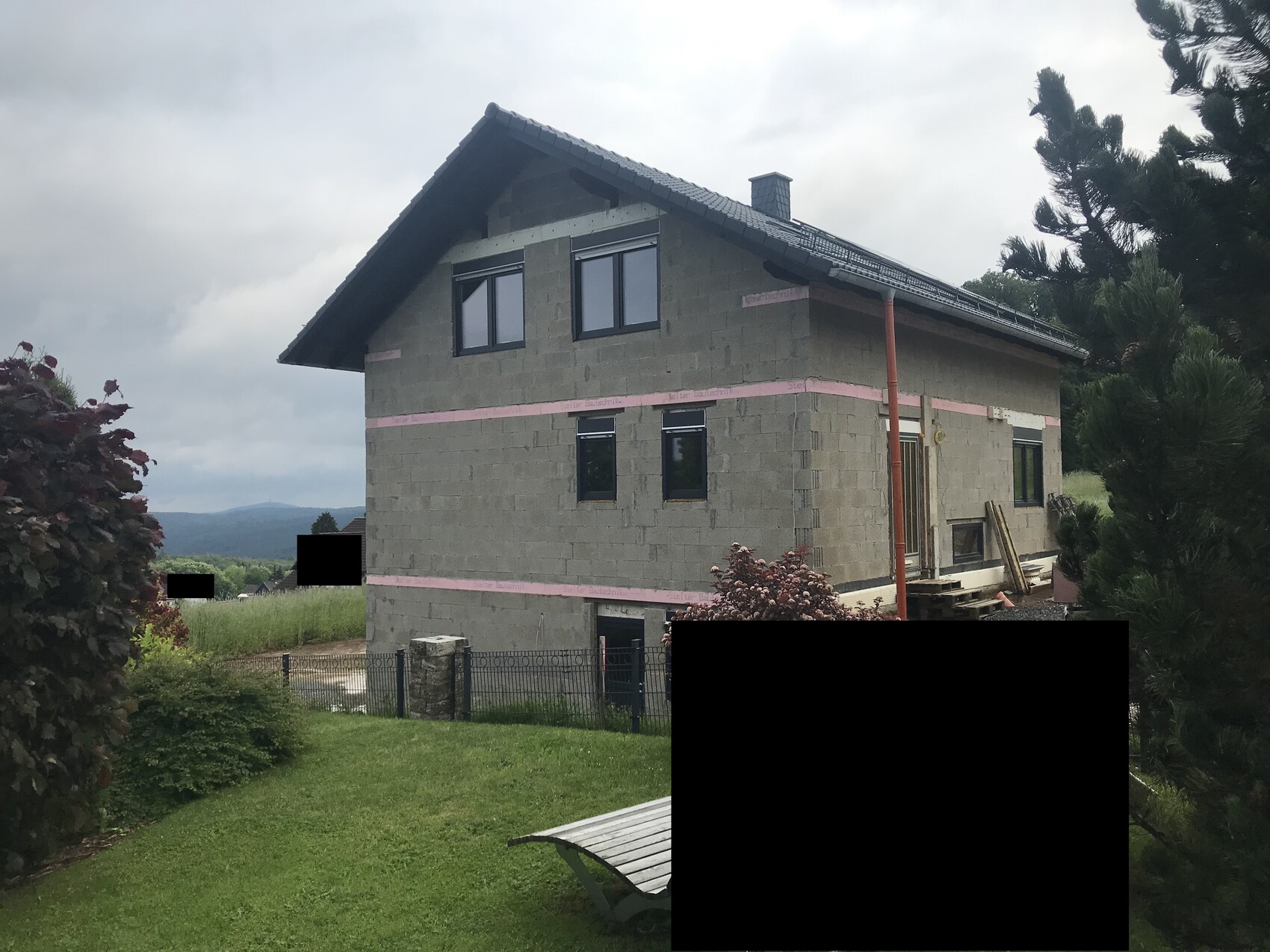 Unfertiges zweistöckiges Betonhaus mit dunklem Dach und Garten im Vordergrund