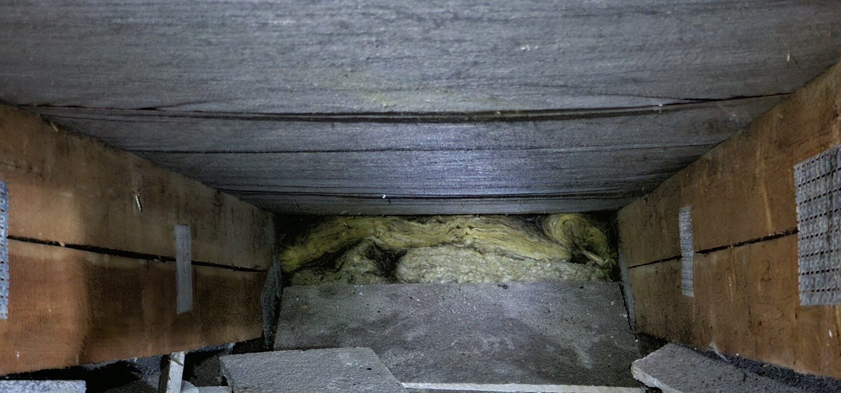 Dark, narrow shaft with brown walls; yellowish fibrous insulation at the end.