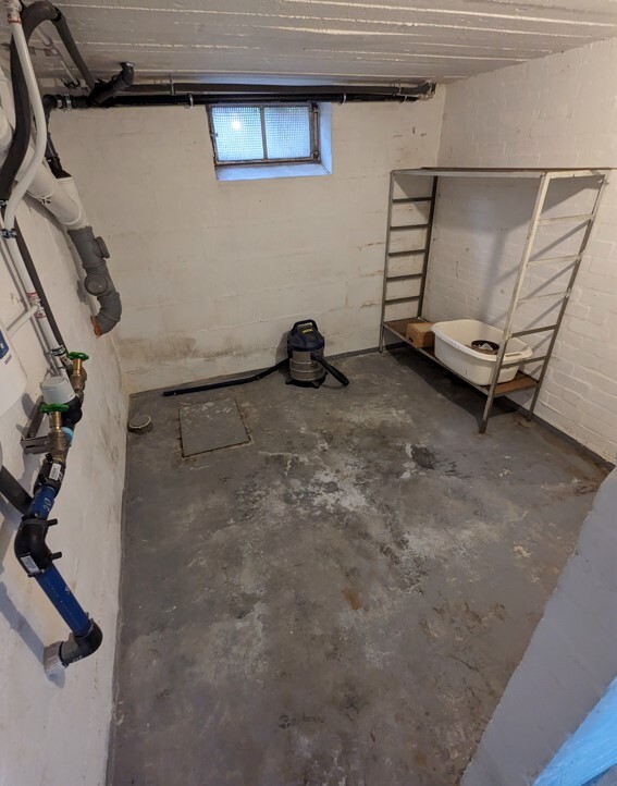 Basement room with pipes, small window, exhaust fan, and shelf with a laundry tub.