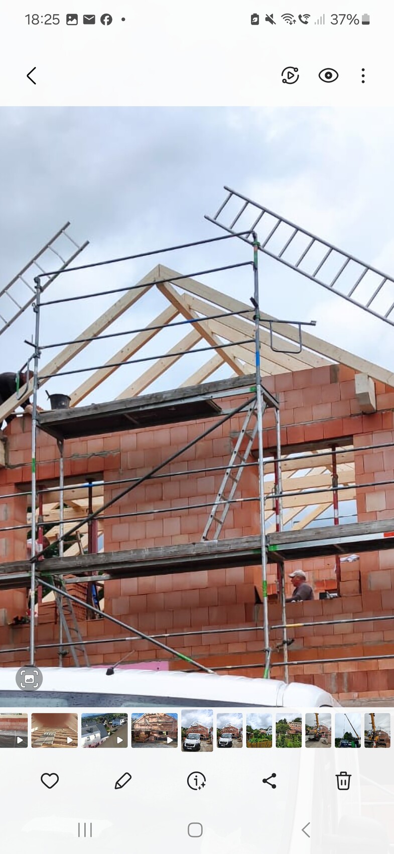 Baustelle mit roter Ziegelwand, Holz-Dachrahmen, Gerüst und Bauarbeiter.